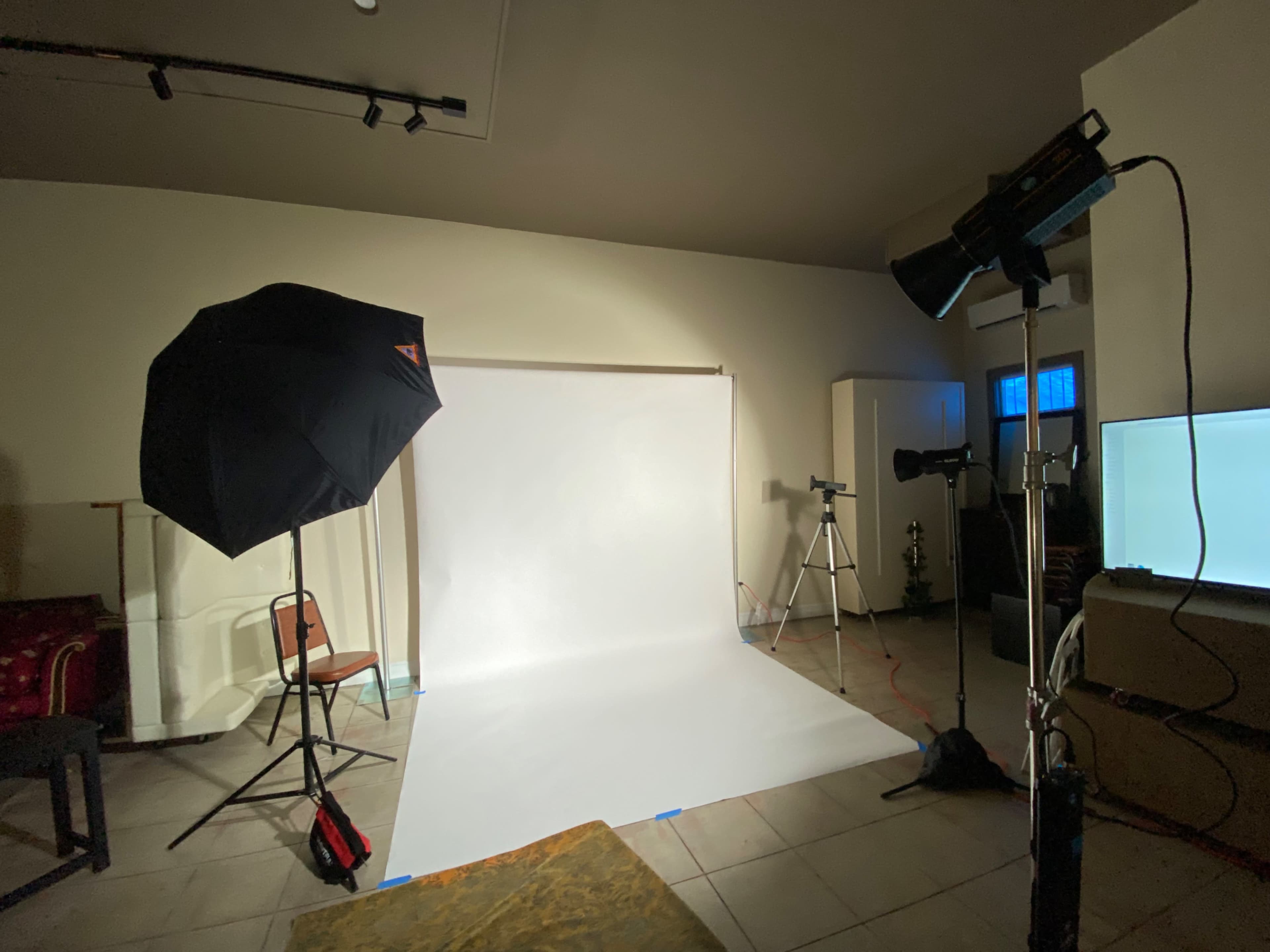 The image shows a photography studio setup featuring a white backdrop, an umbrella light, and a studio monitor.