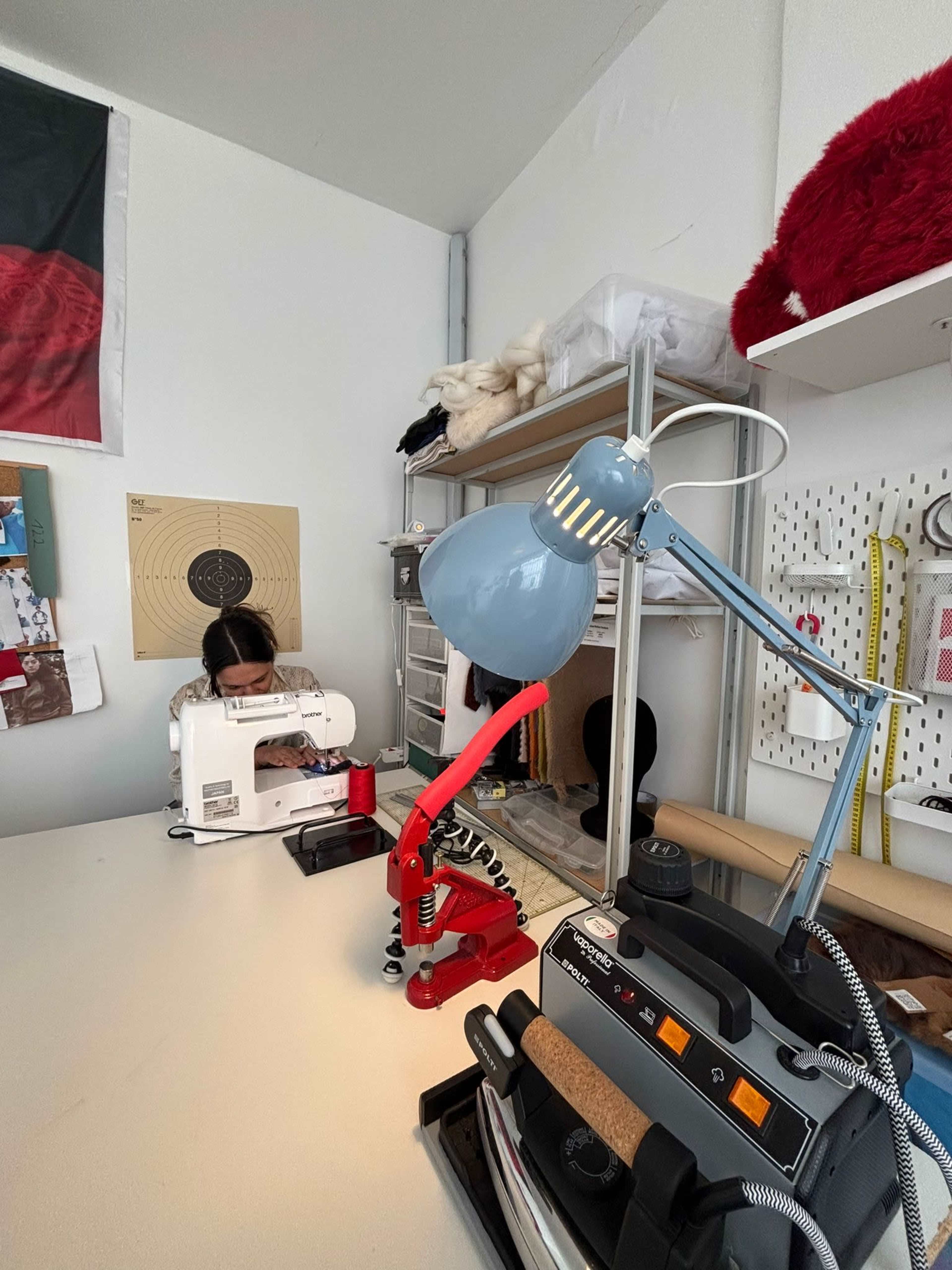 A person is seated at a sewing machine in a well-organized workspace featuring various tools and equipment.