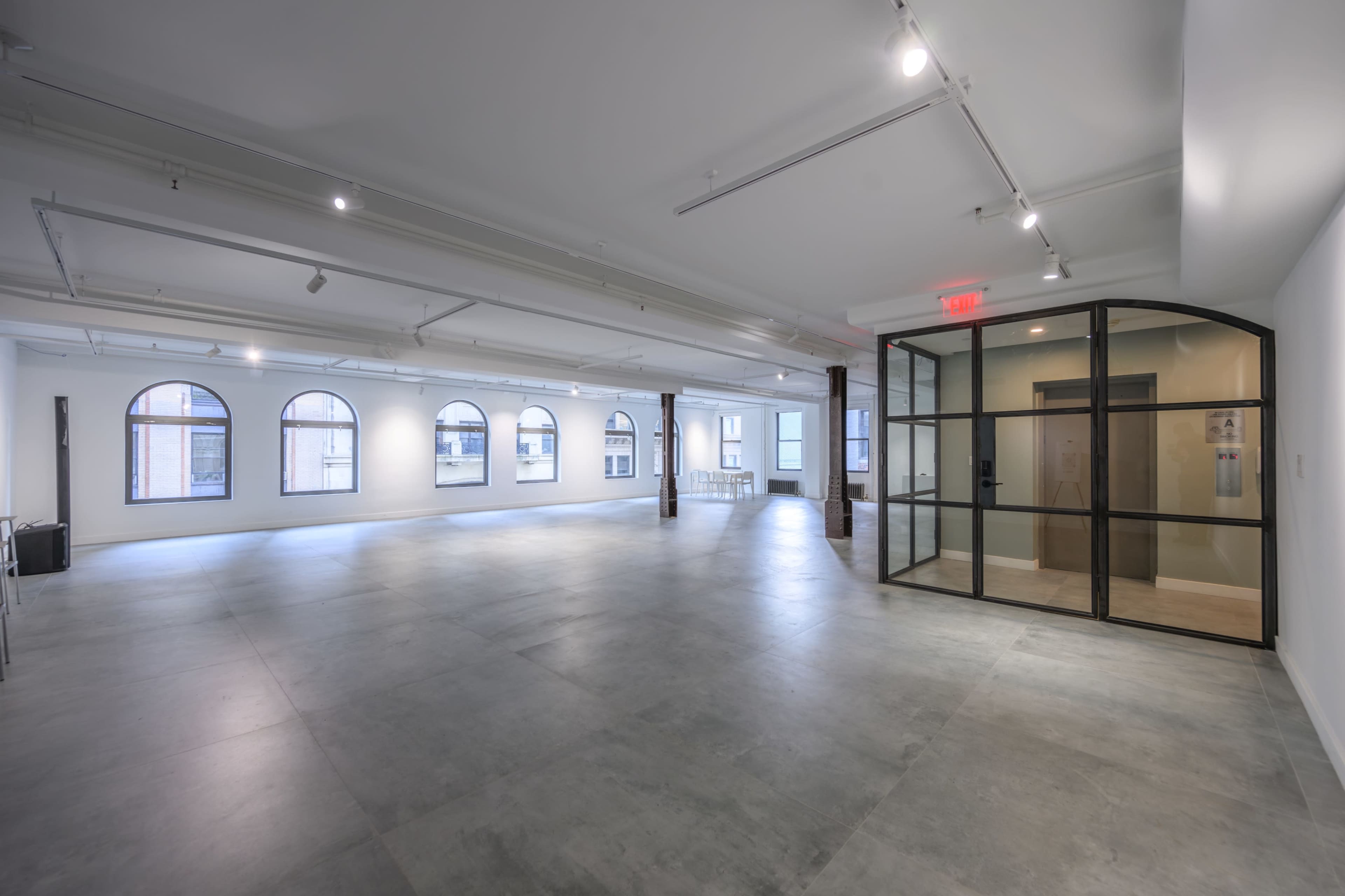 The image shows a spacious, modern interior featuring polished concrete floors, large arched windows, and a glass-walled office area.