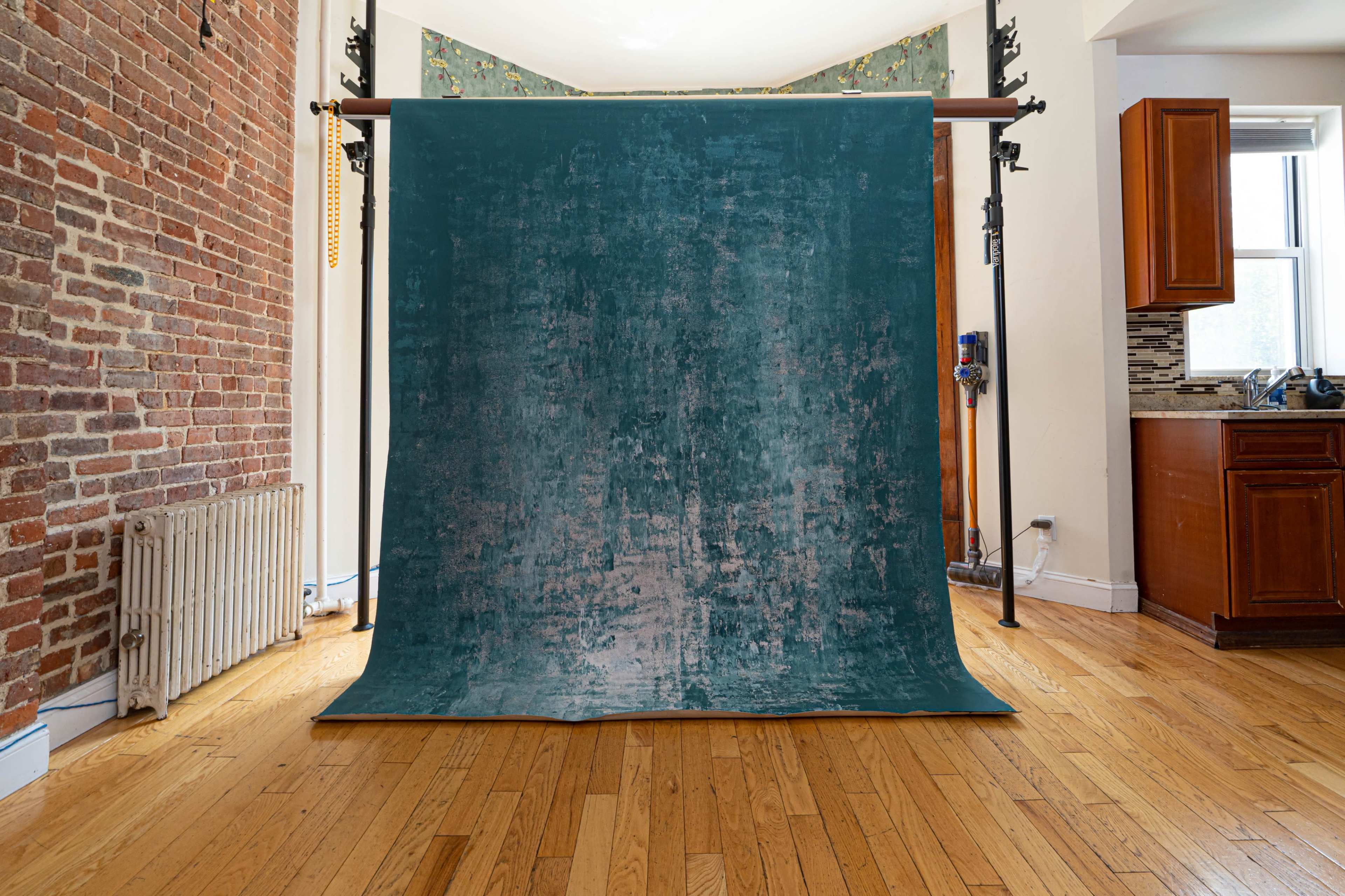 A large blue backdrop is set up in a room with hardwood floors and exposed brick walls, with a kitchen area visible in the background.