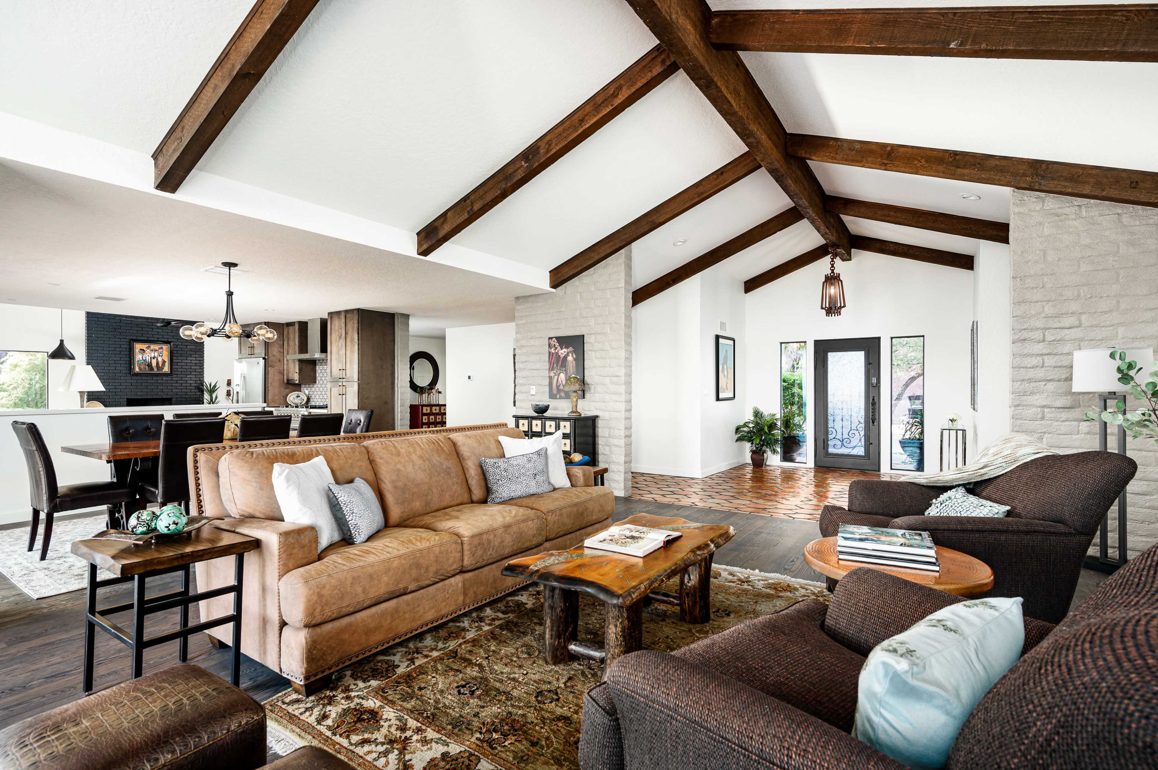 The living room features a combination of a brown leather sofa and two upholstered chairs, with wooden beams overhead and a stone wall.