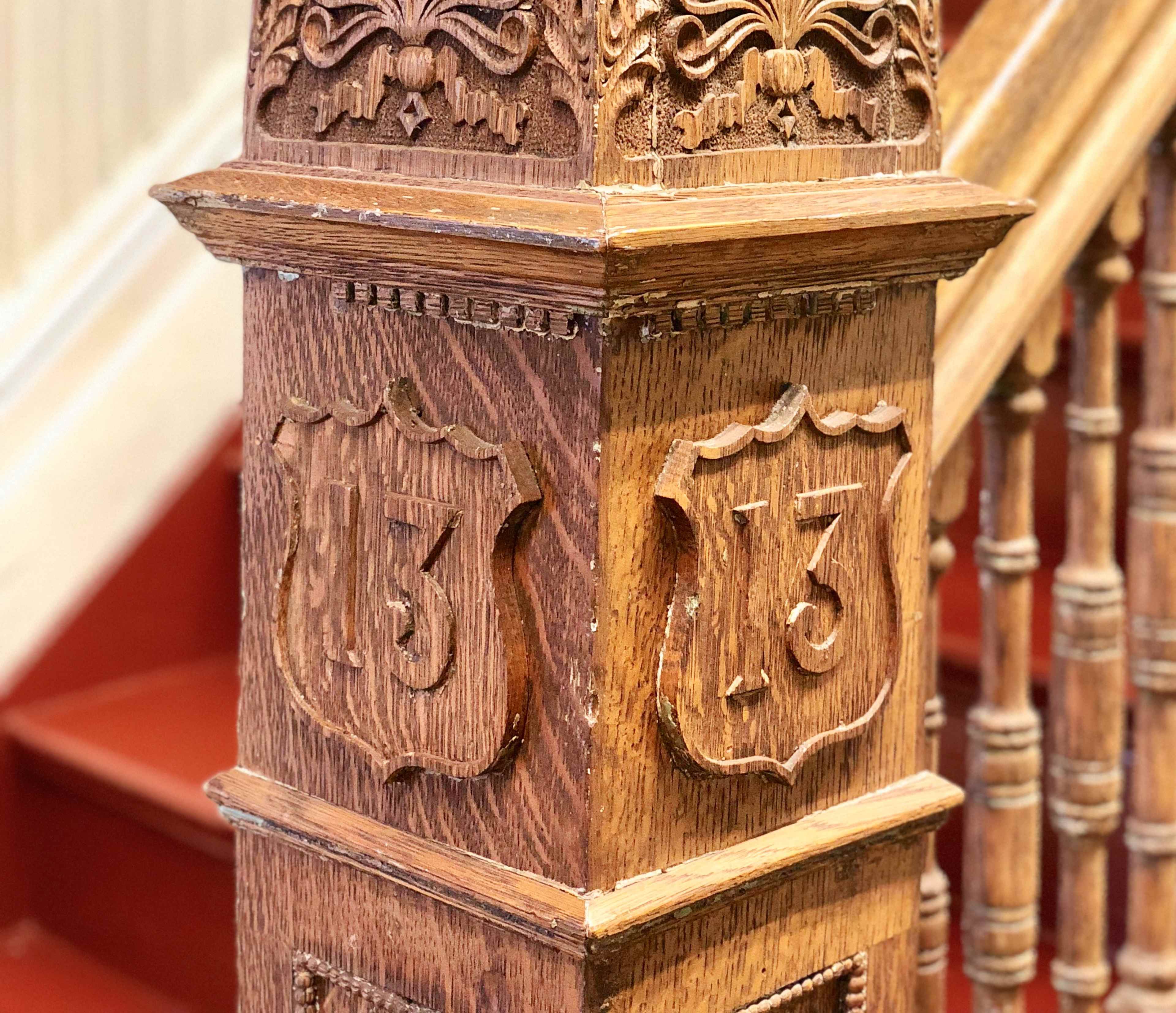 A carved wooden post with the number "13" prominently displayed on it, positioned near a staircase with red carpeting.