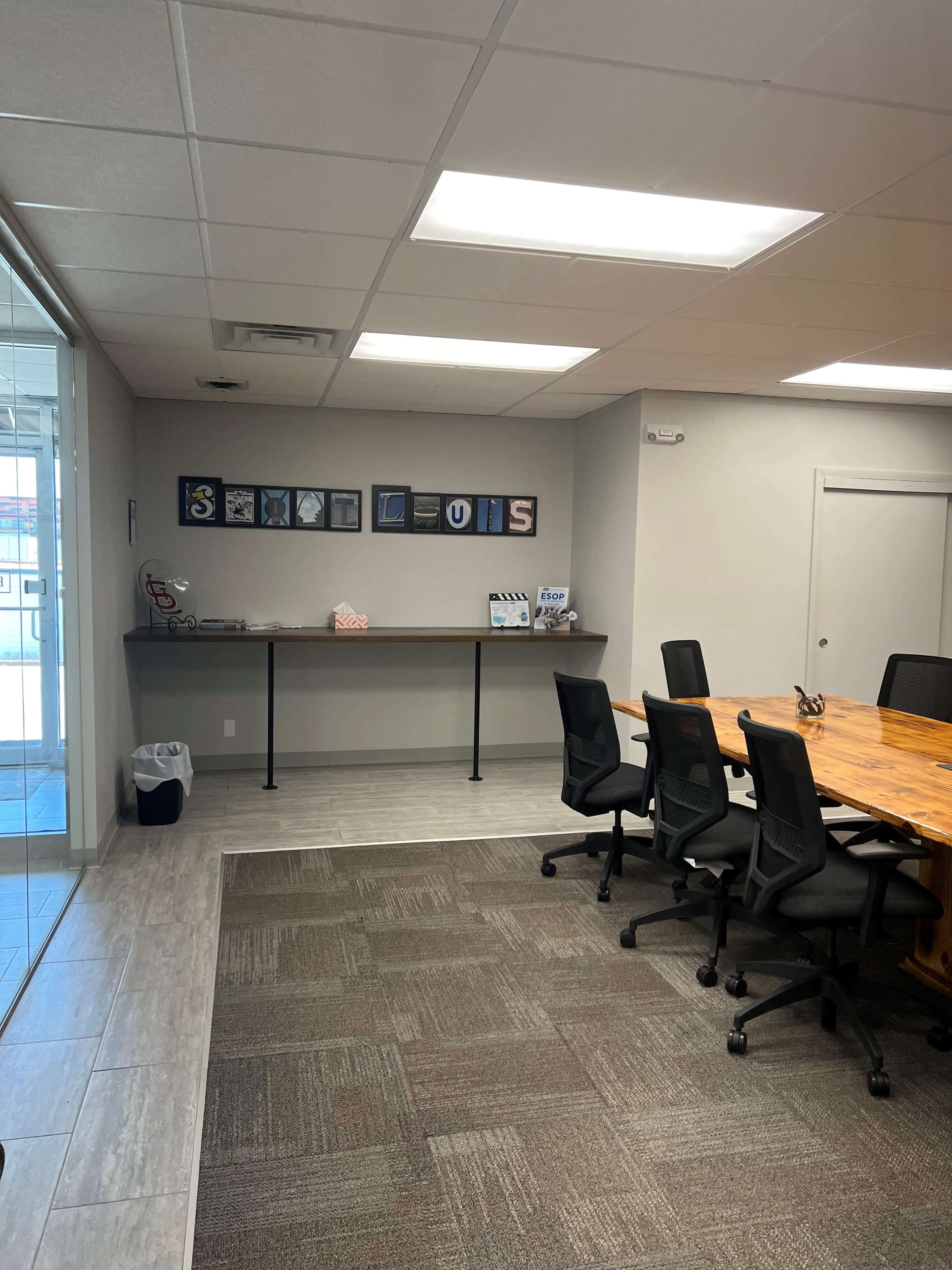 A modern conference room features a long table surrounded by black chairs, with a display of framed letters on the wall spelling "ST. LOUIS."