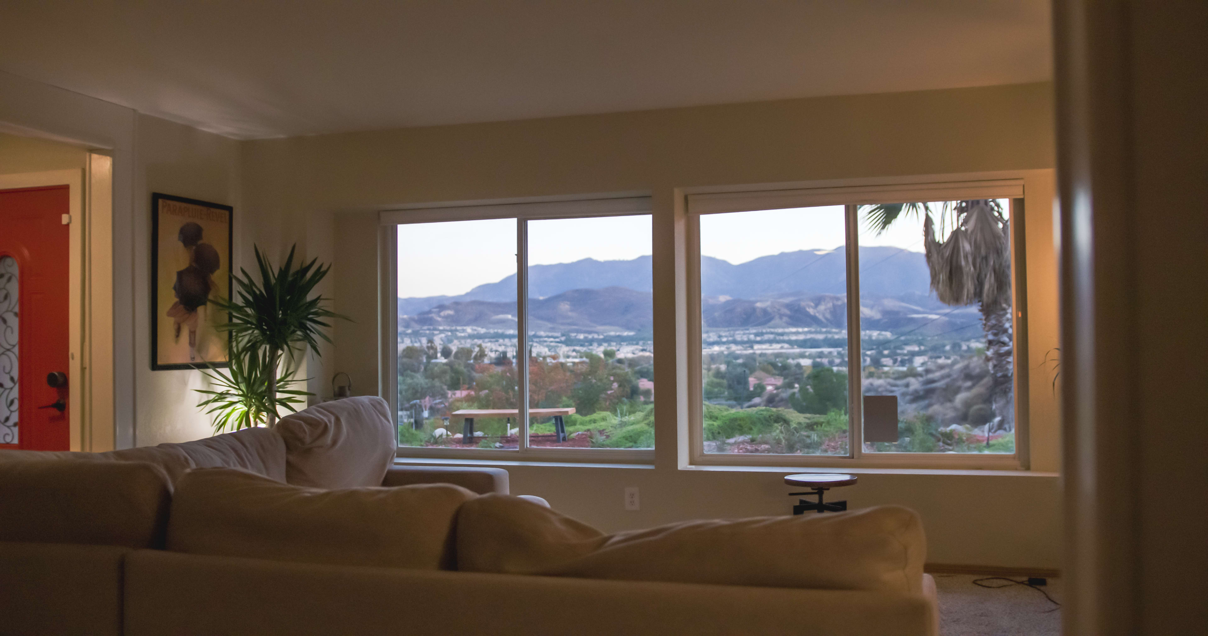 A cozy living room features a large window with a view of mountains and greenery.