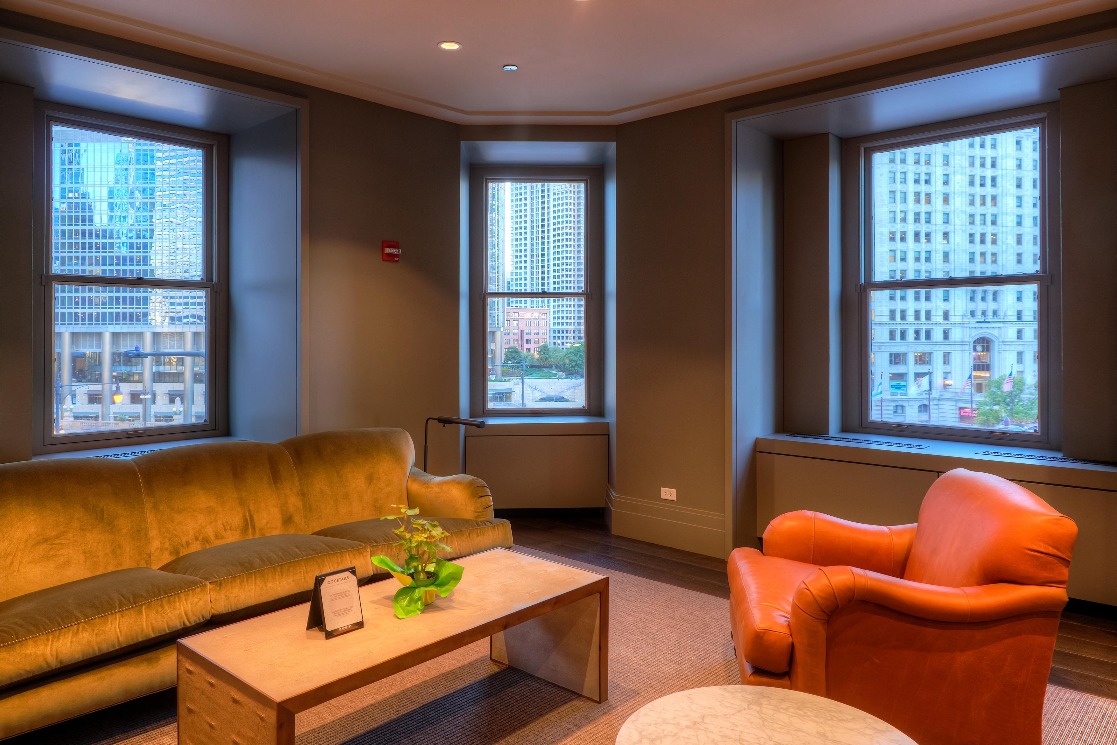 A green sofa and an orange armchair are positioned in a room with large windows overlooking a cityscape.