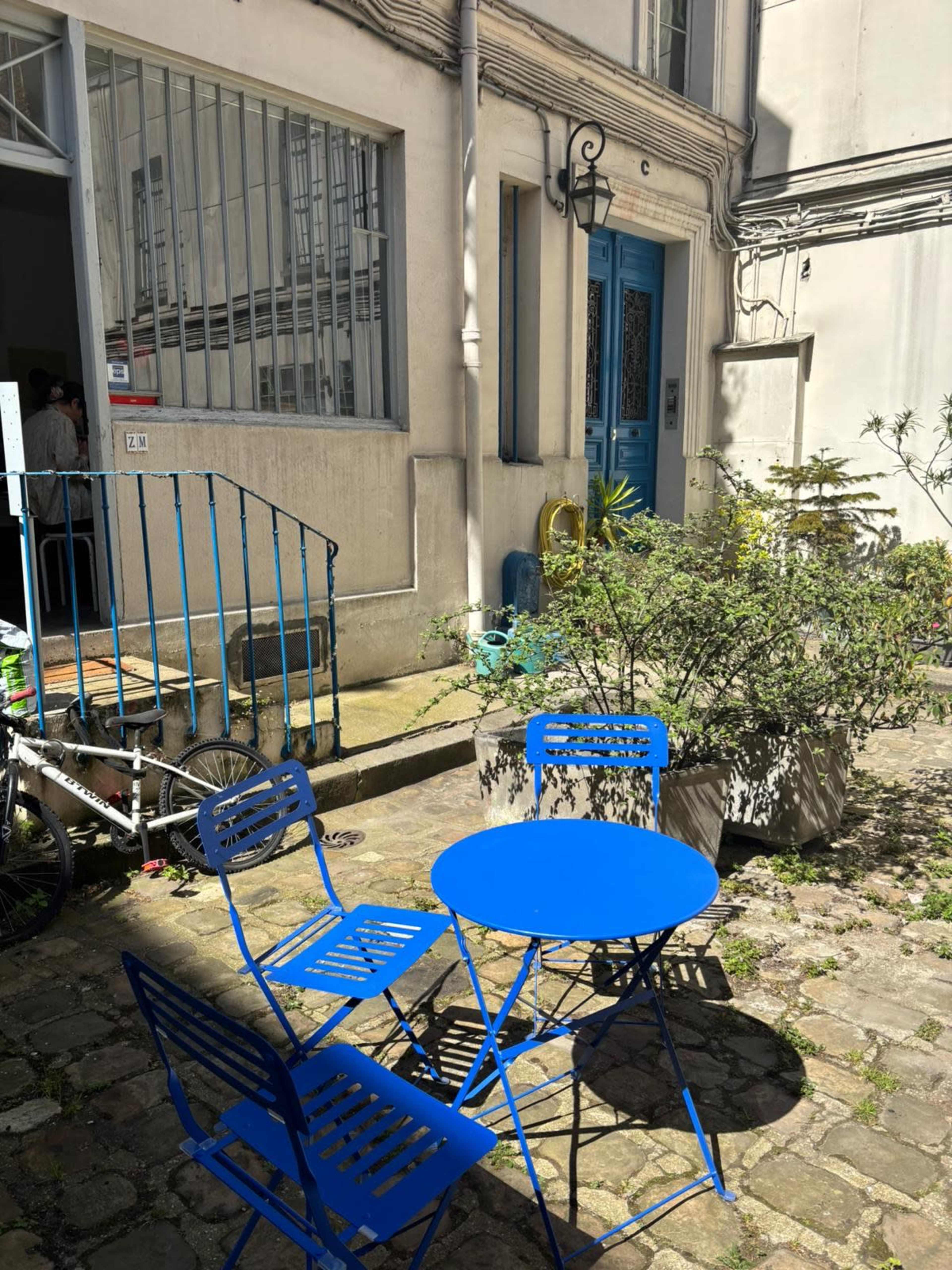 A small outdoor courtyard features a blue table and chairs surrounded by plants and stone paving.