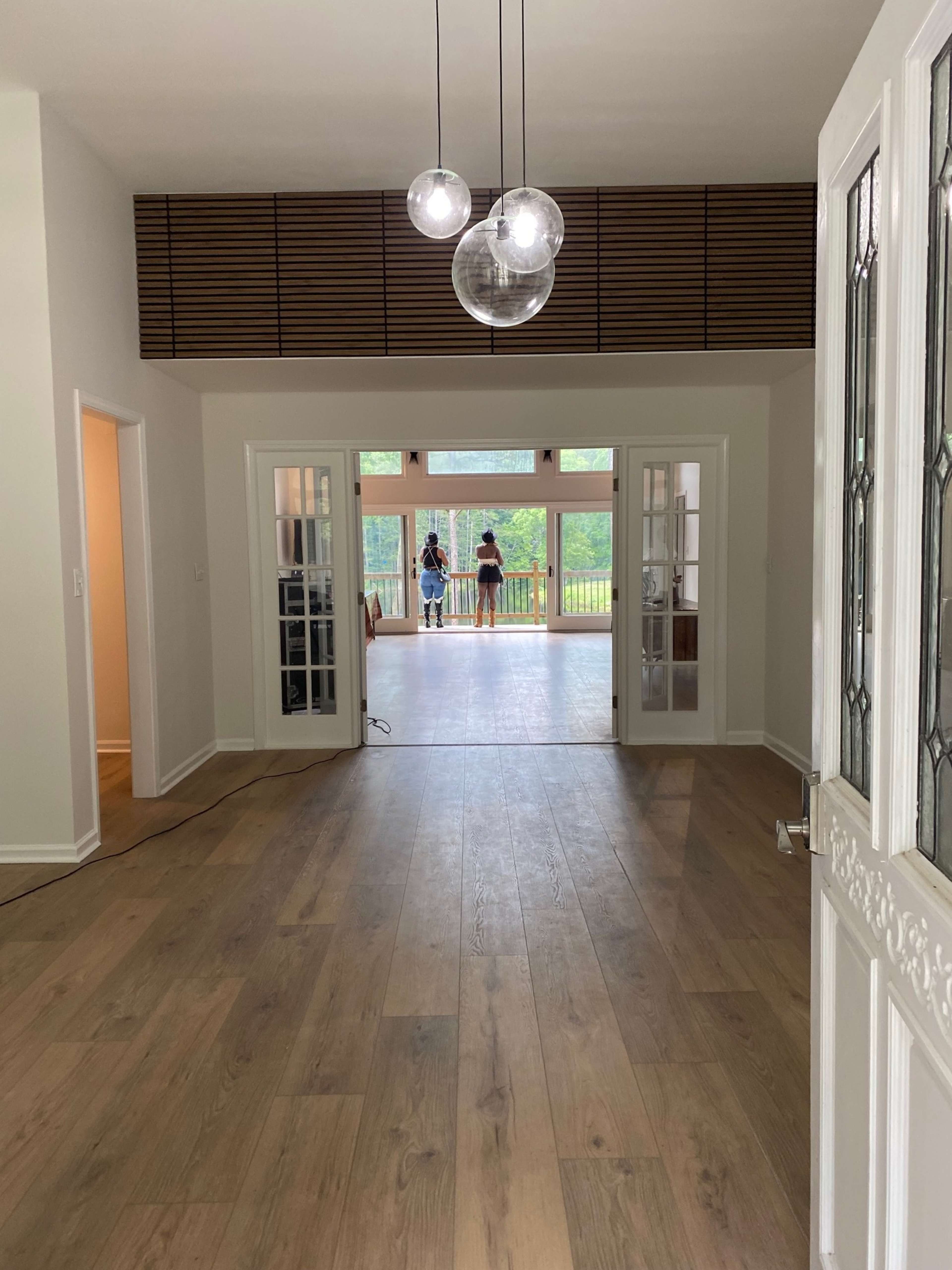 The image shows a spacious, well-lit interior that opens to a large outdoor area, with wooden flooring and glass doors leading to a balcony.