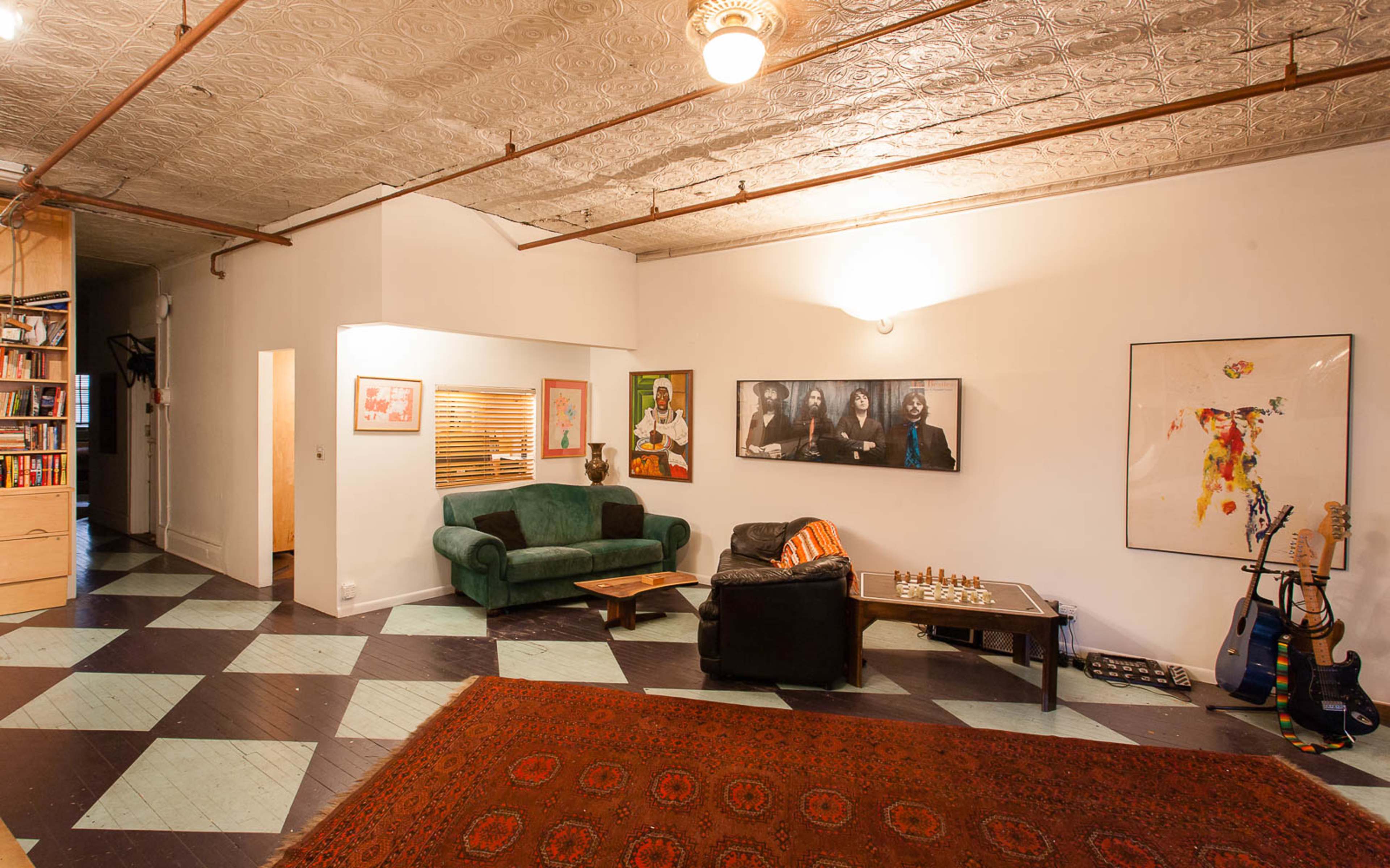 A spacious living room with patterned flooring, a green couch, a black armchair, a coffee table, and various artworks on the walls.