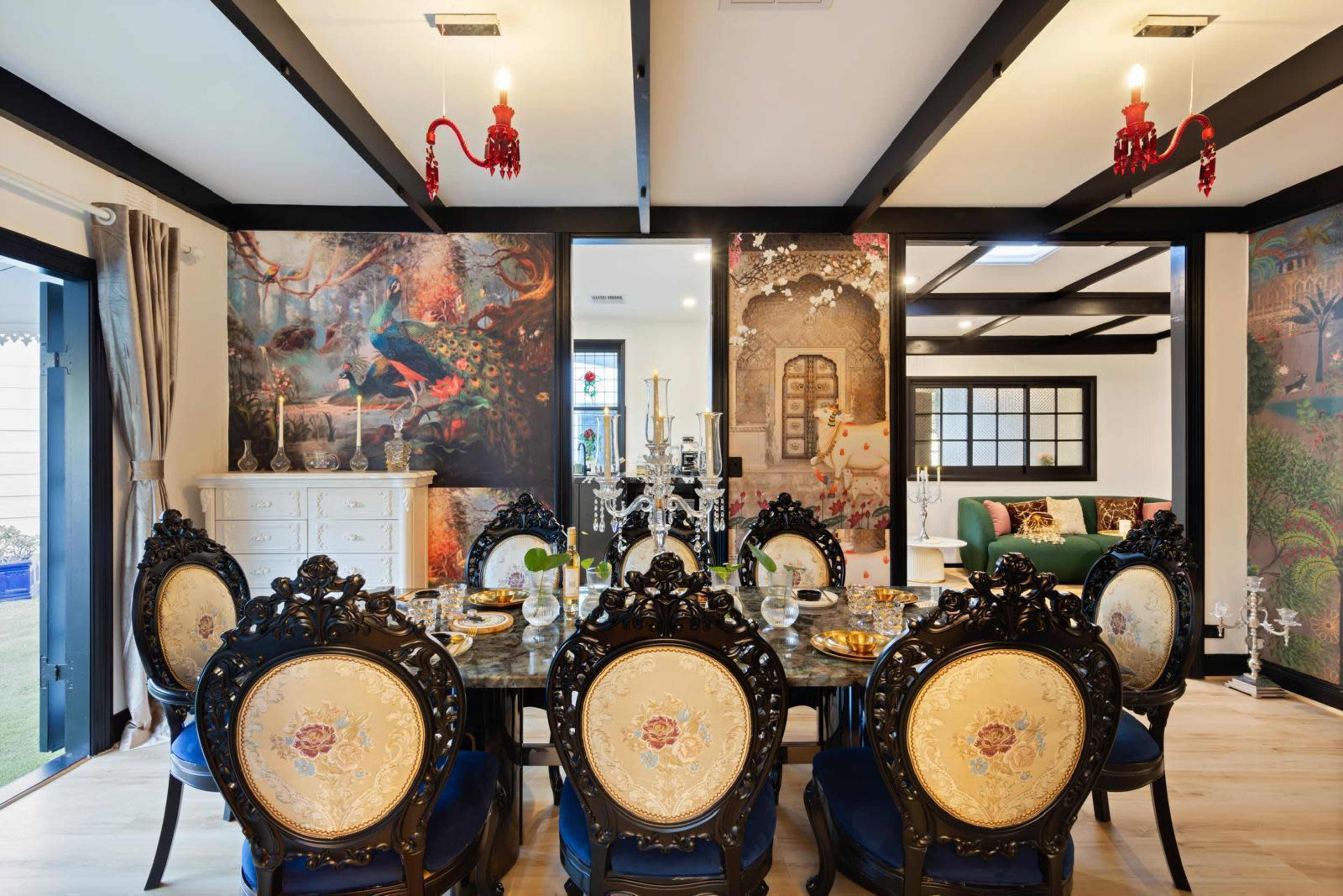 The image shows an elegant dining room featuring a large table surrounded by ornate chairs, with colorful wall murals and decorative lighting overhead.