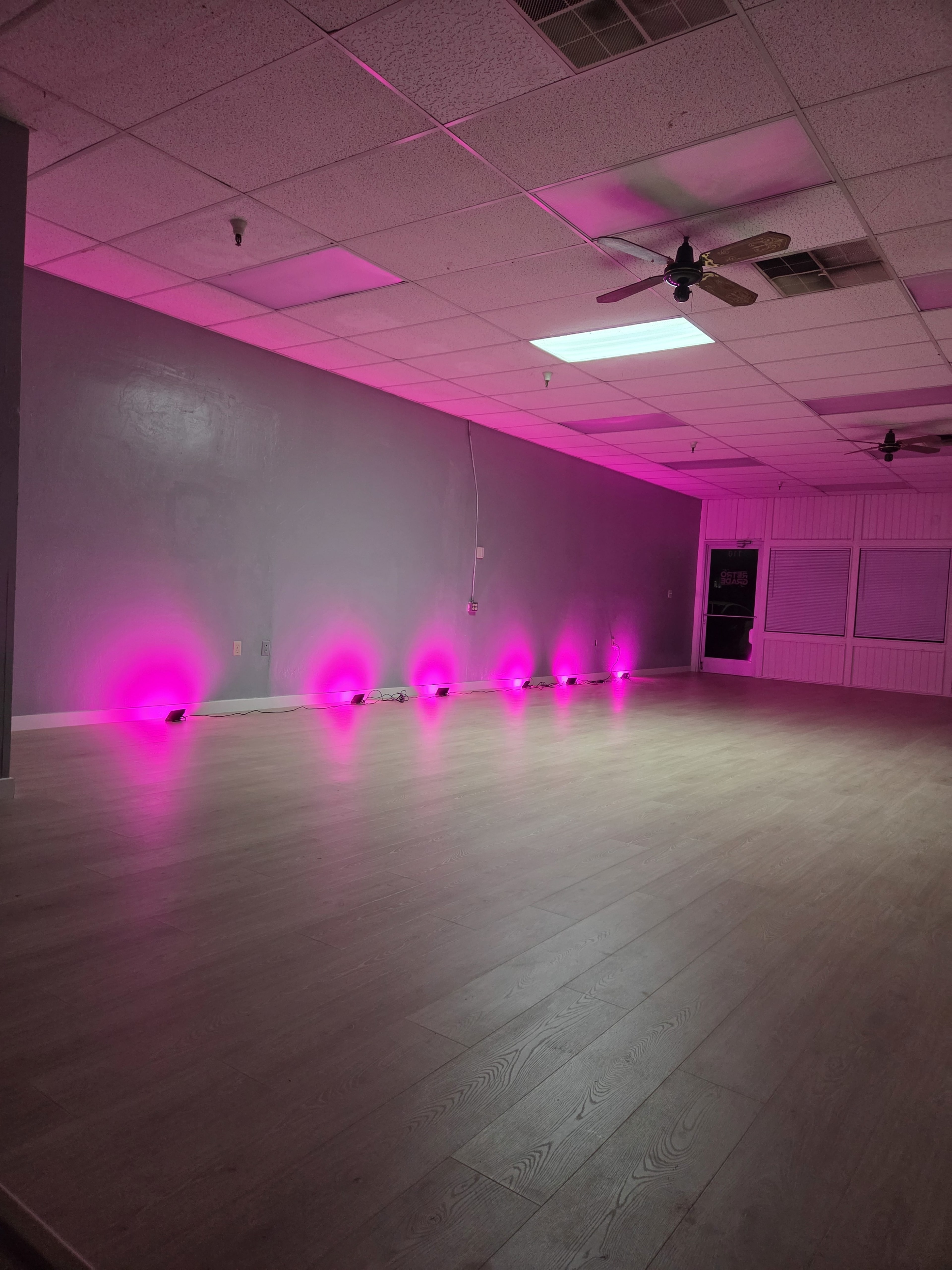 The image shows a spacious room with wooden flooring and pink lighting along the walls.