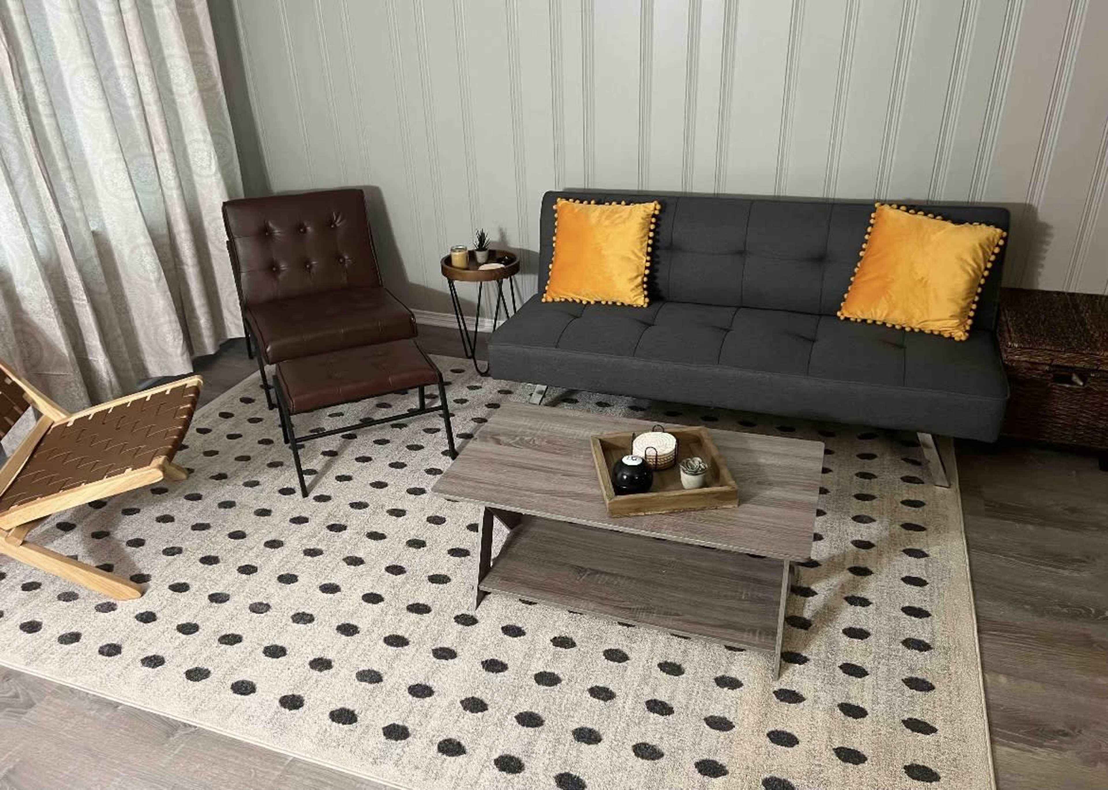 A modern living room setup with a gray sofa, a brown chair, a round side table, and a patterned area rug.