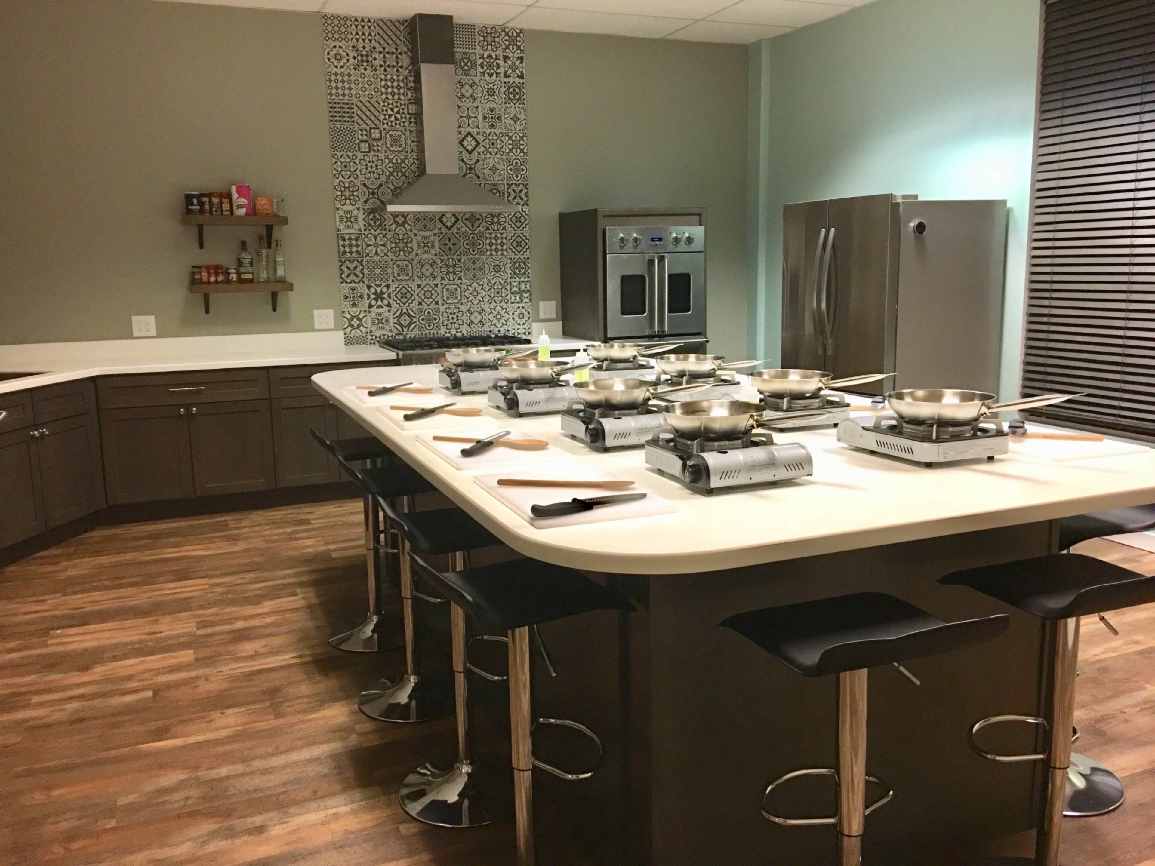 A modern kitchen space with a large island, multiple cooking stations, stainless steel appliances, and a patterned backsplash.