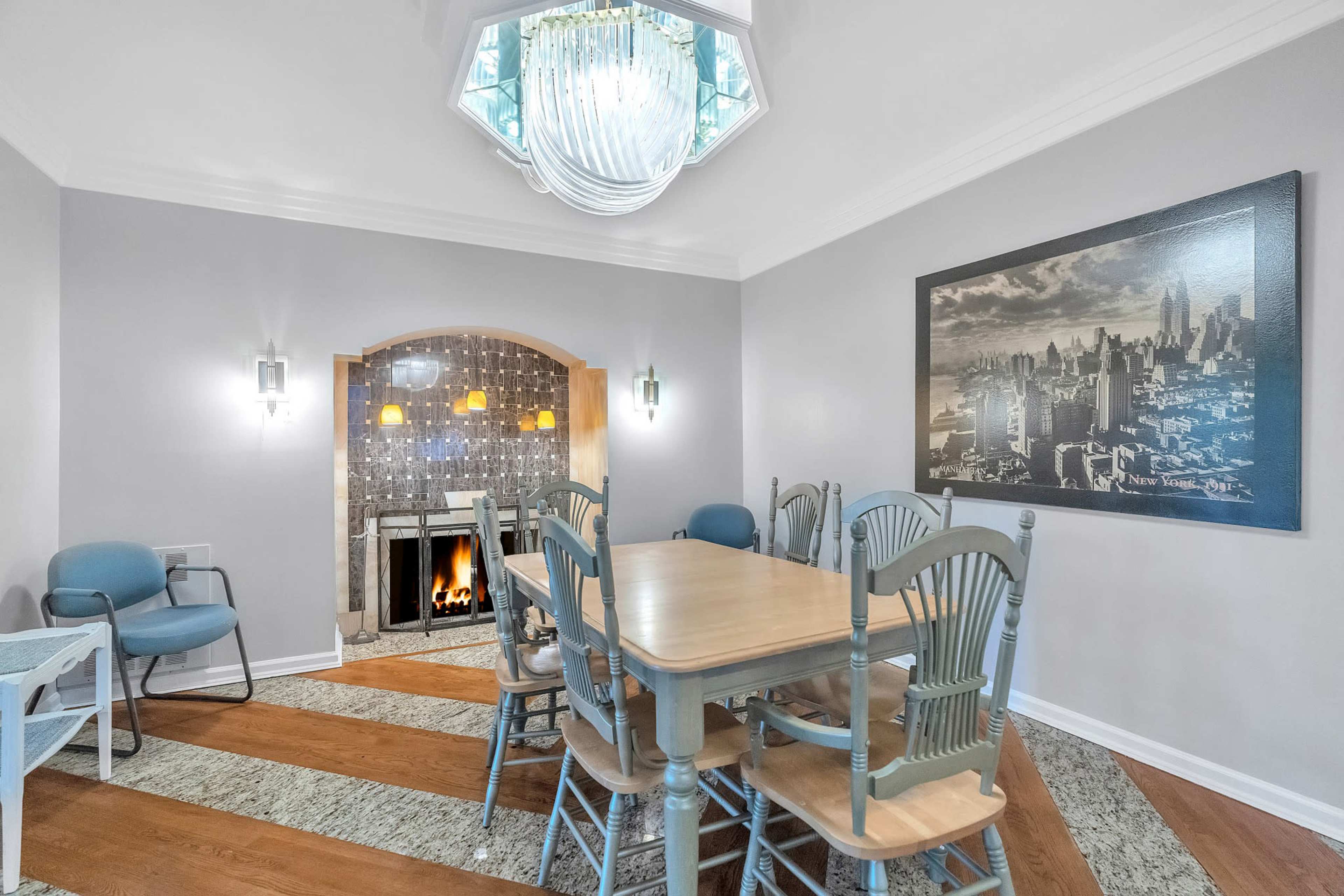 A dining area features a wooden table surrounded by six chairs, with a decorative fireplace and a large cityscape photograph on the wall.