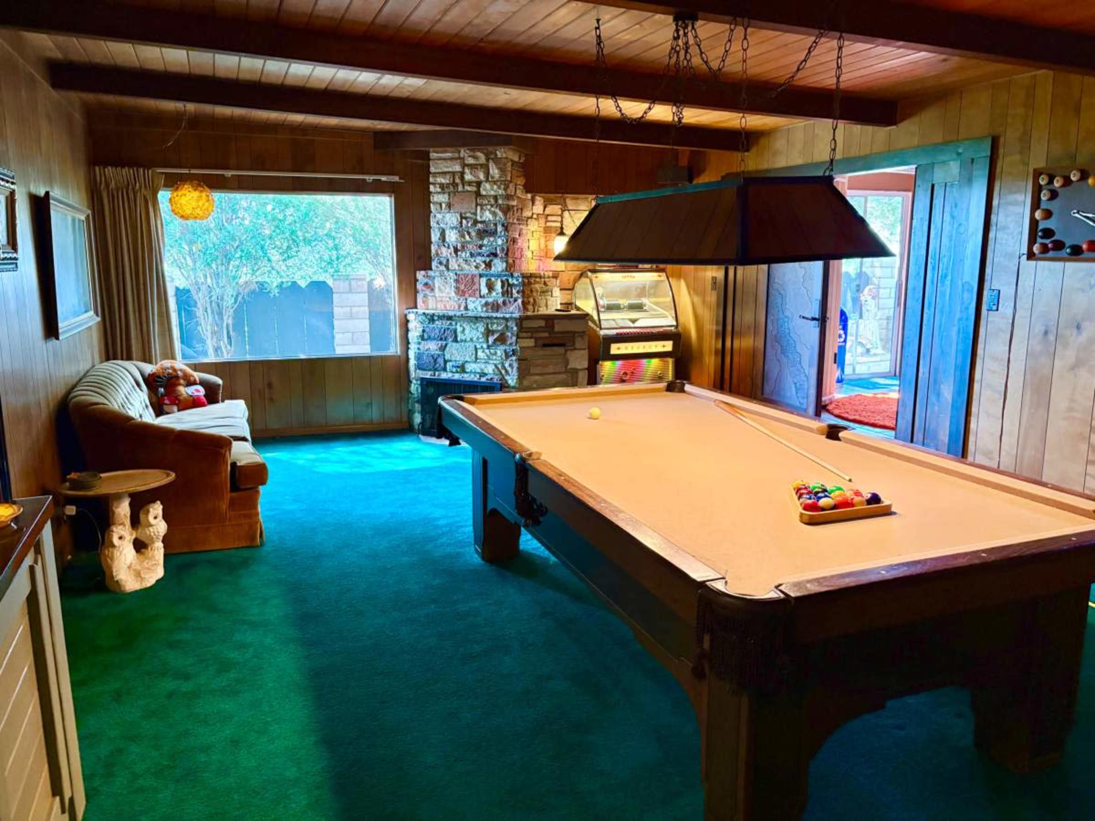 A cozy game room features a billiards table, a stone fireplace, and a sofa by a window.