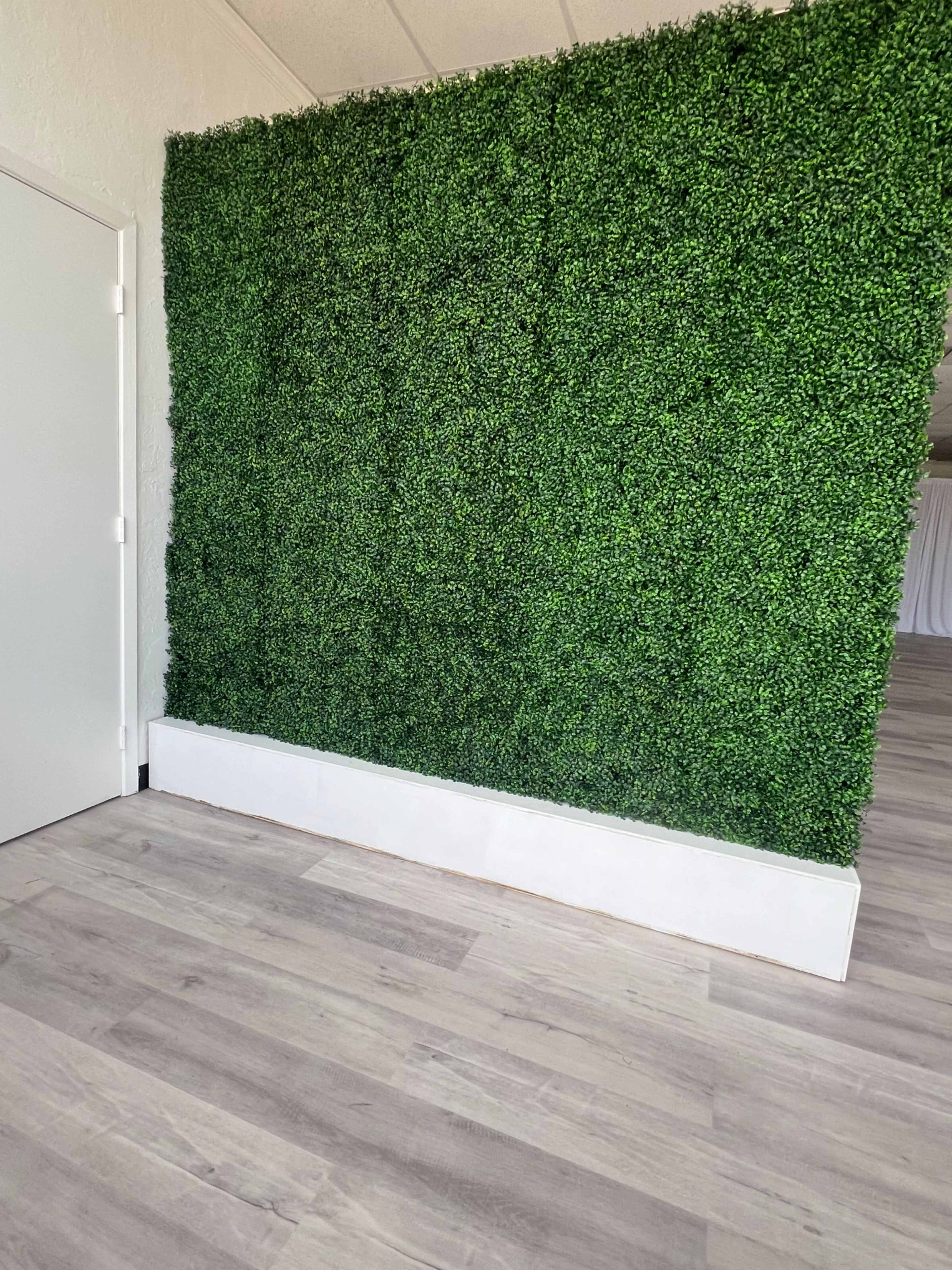 A wall covered with artificial greenery in a room with light wood flooring.