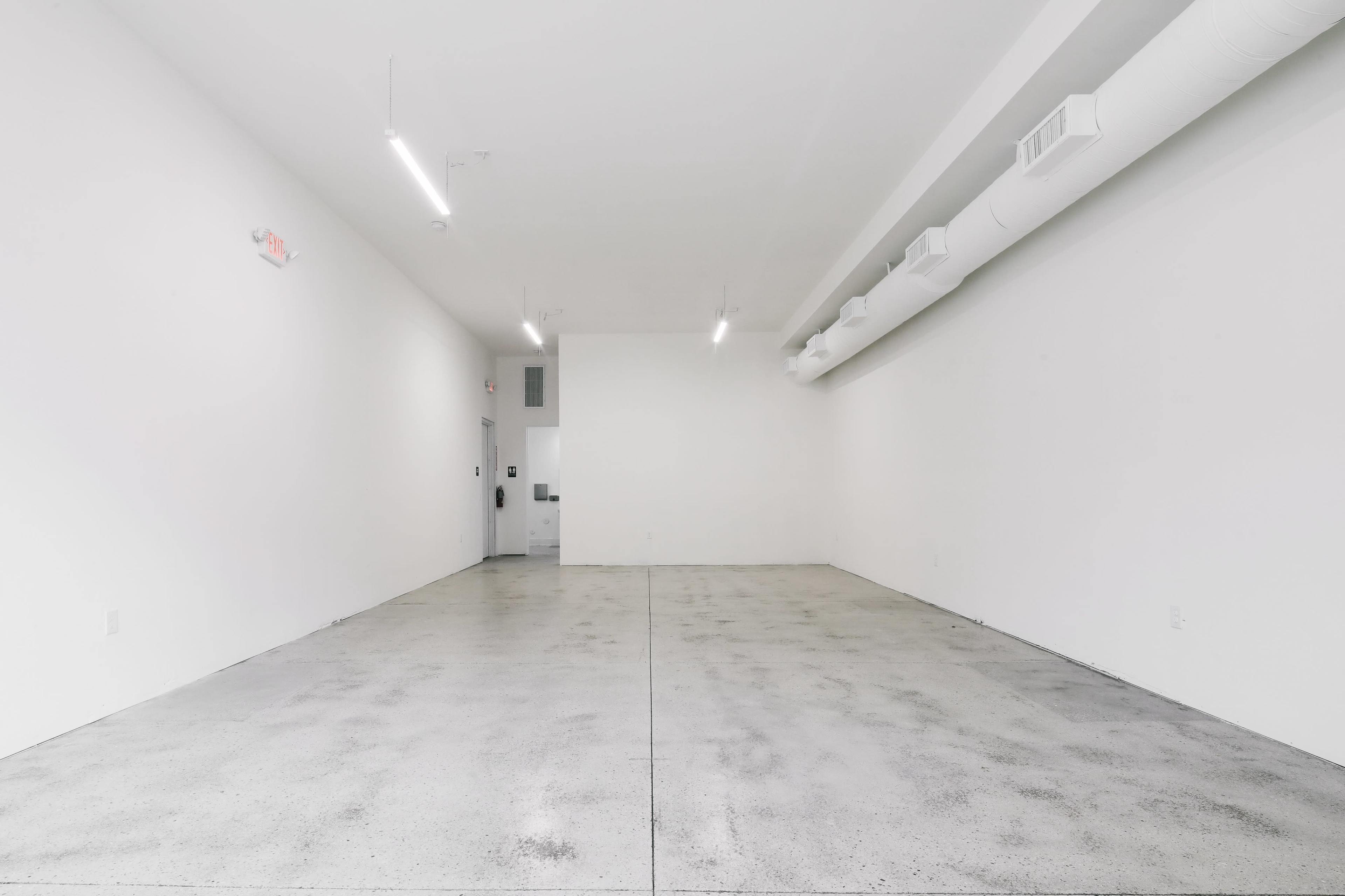 An empty room with white walls, a concrete floor, and overhead lighting.
