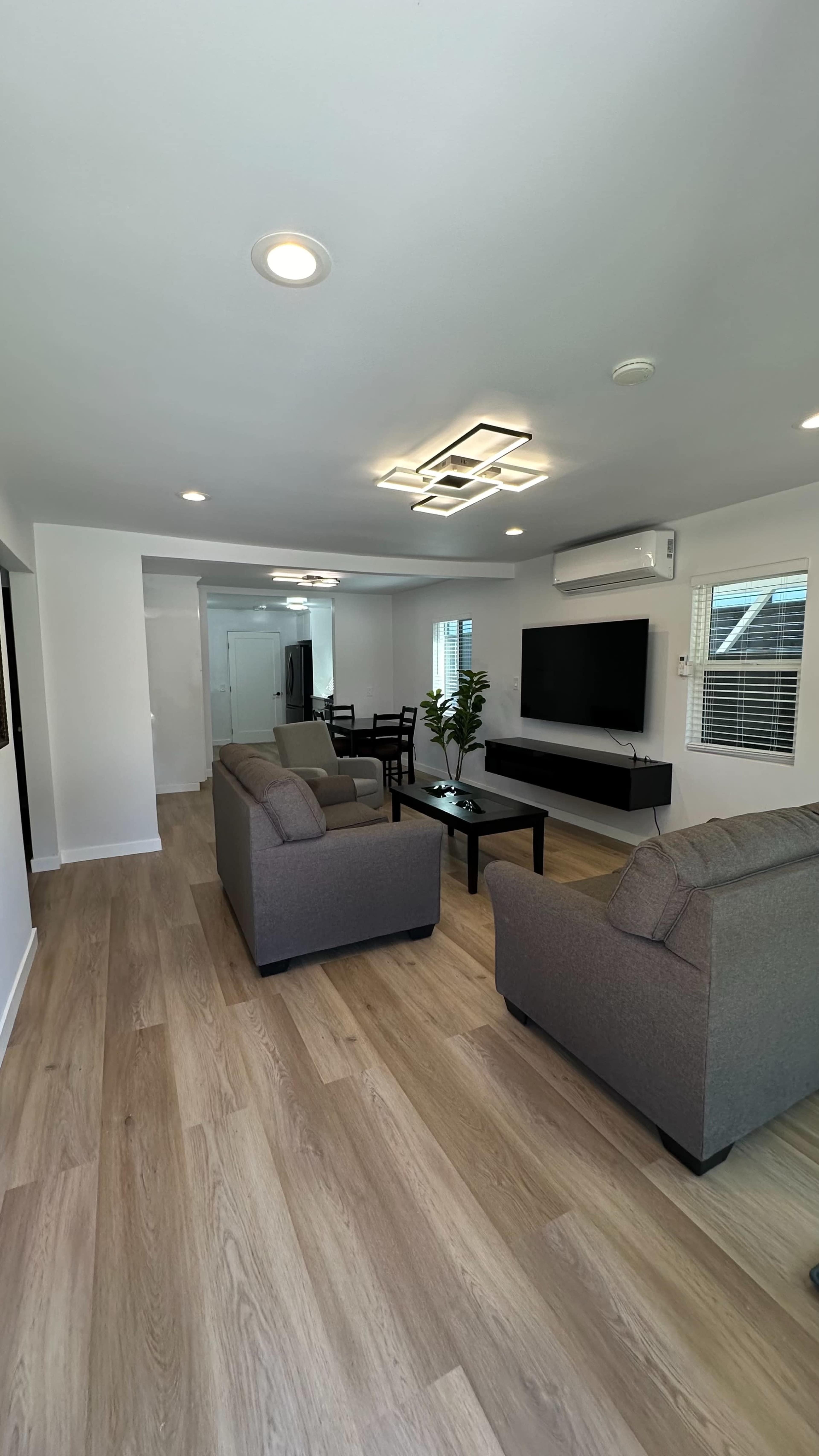 A modern, open-concept living area with two gray sofas, a coffee table, and a wall-mounted television.