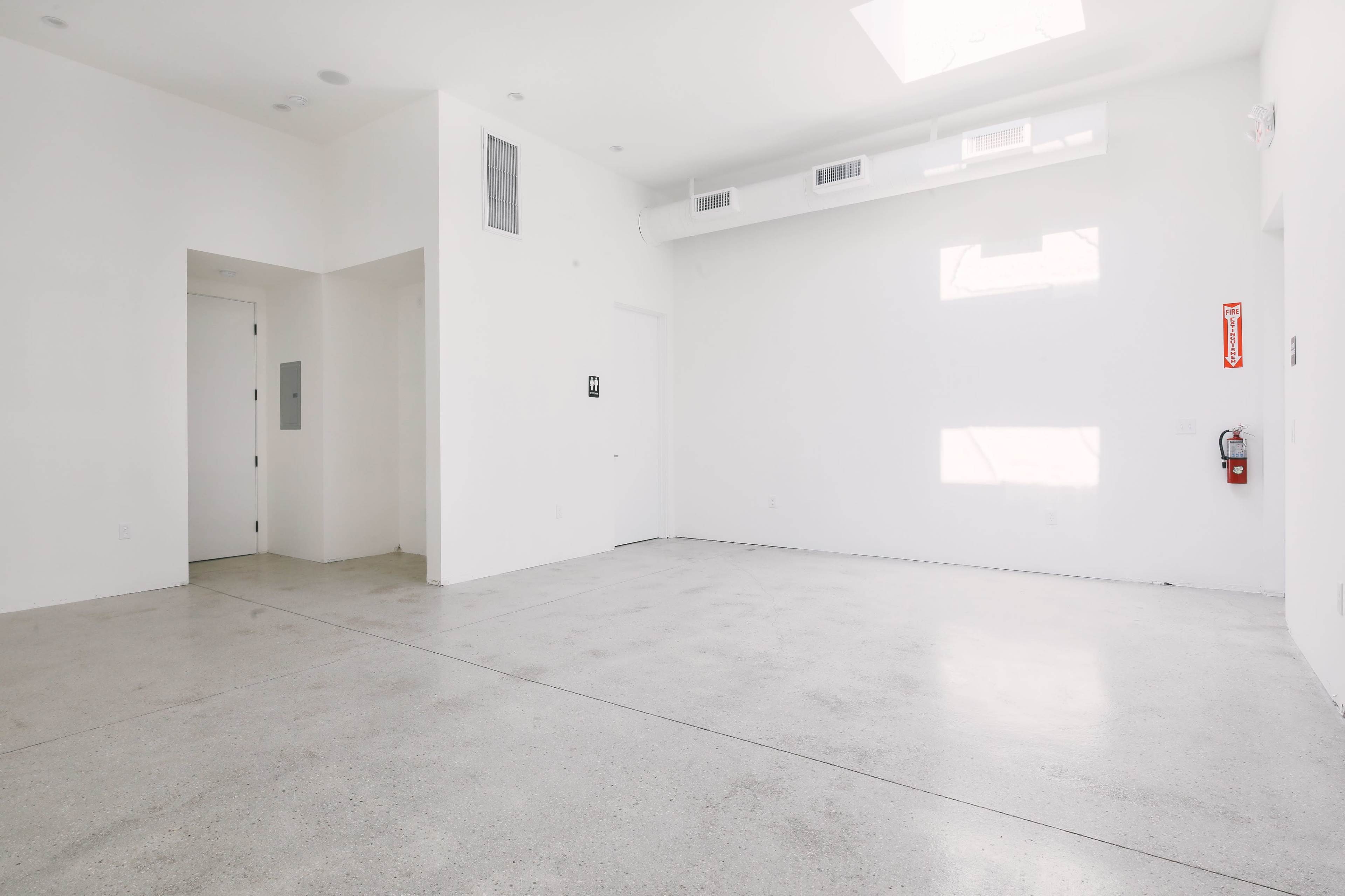 A spacious, empty room with white walls, a concrete floor, and a ceiling that features a skylight.