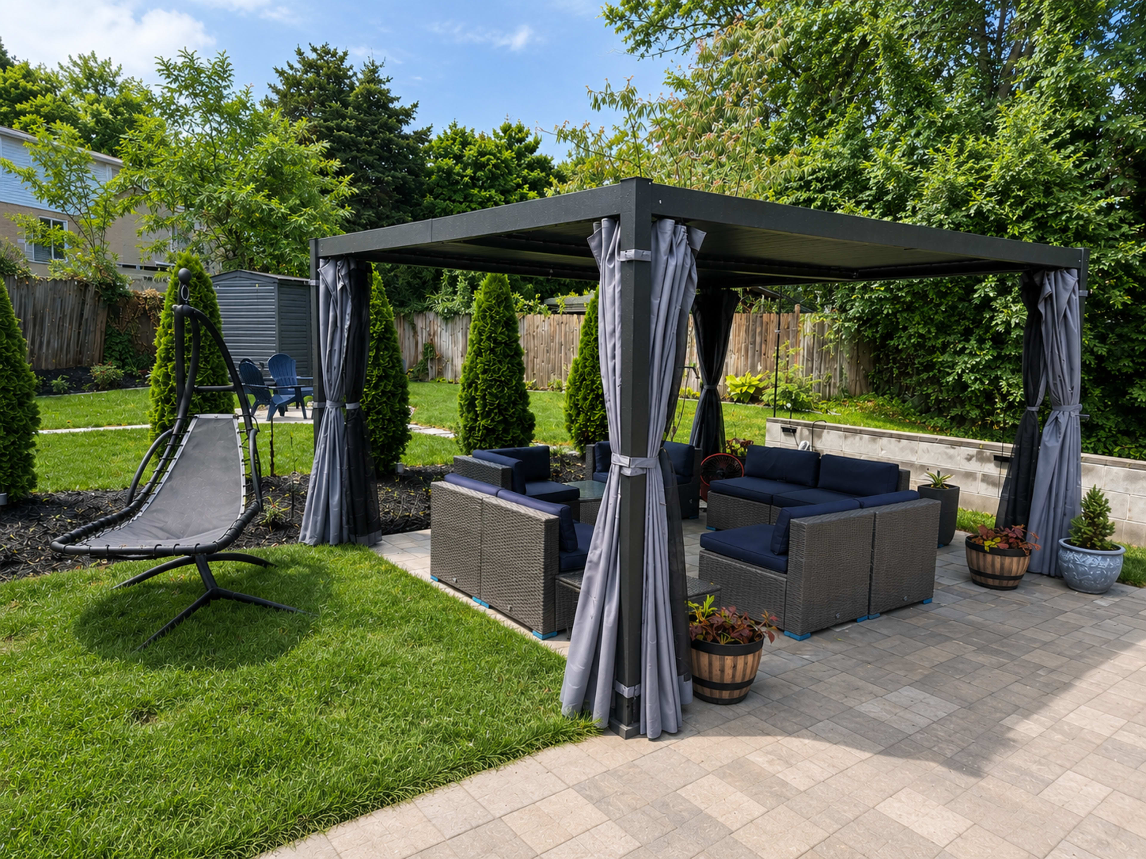 A shaded outdoor patio area features a black pavilion with gray curtains, wicker furniture, and neatly trimmed shrubs.