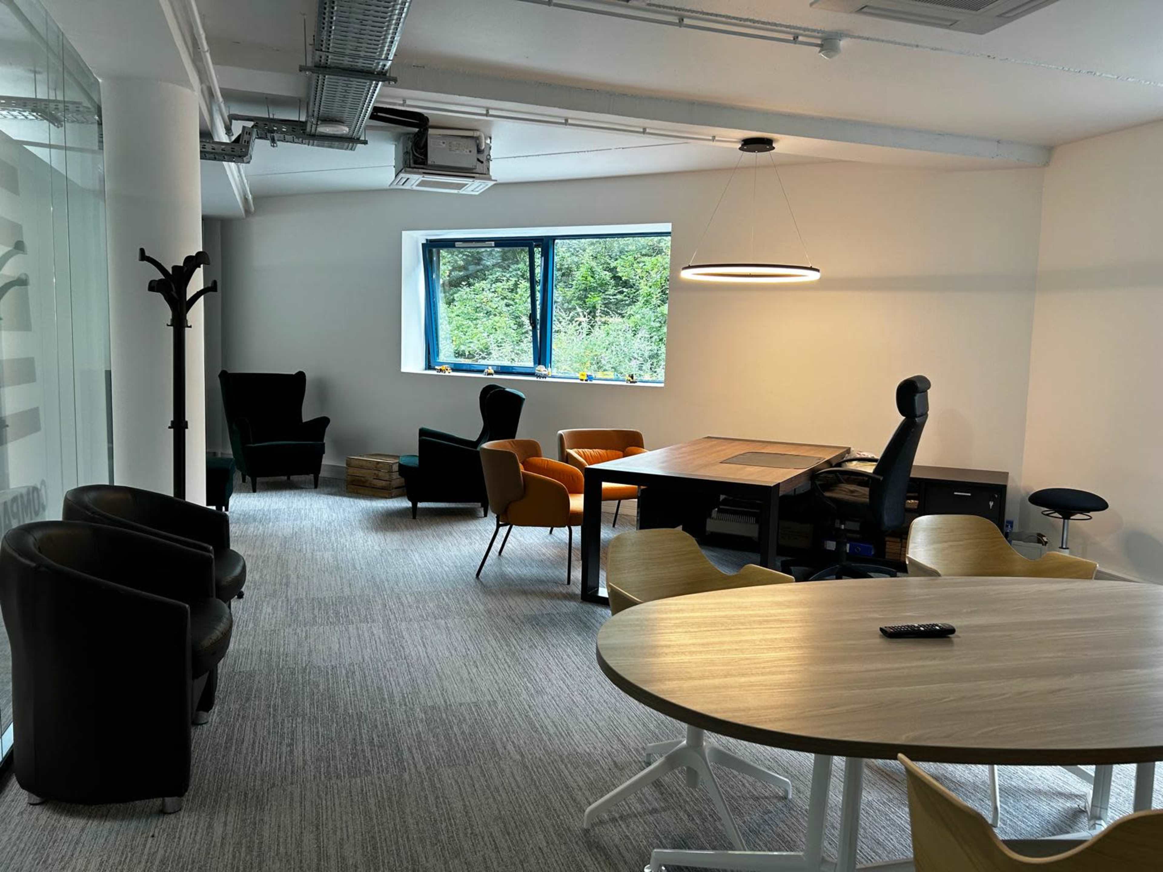 The image shows an office space featuring a mix of seating arrangements, a large desk, and a window with natural light.