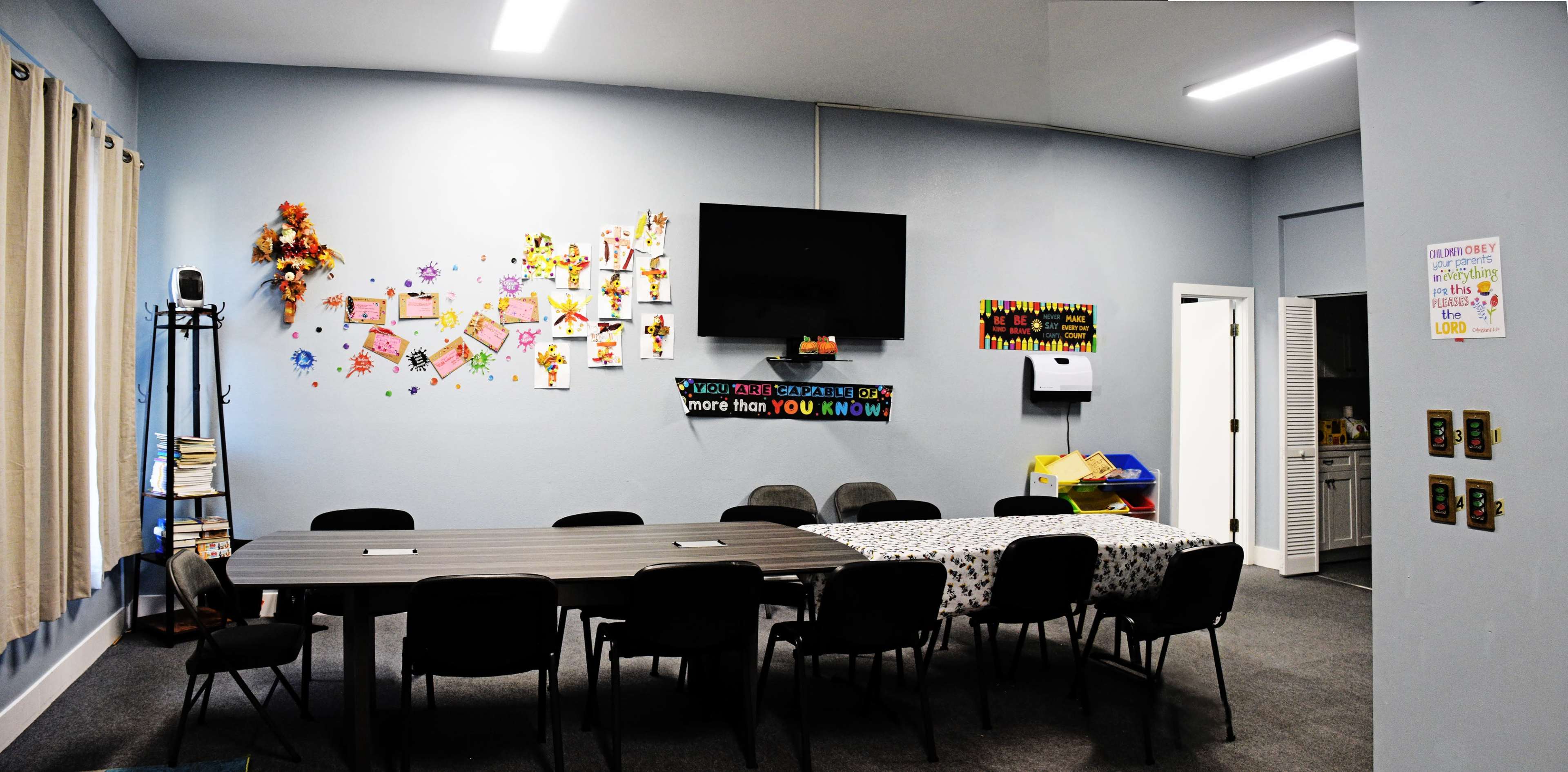A rectangular table with chairs is positioned in a room adorned with colorful decorations, a wall-mounted TV, and various wall hangings.