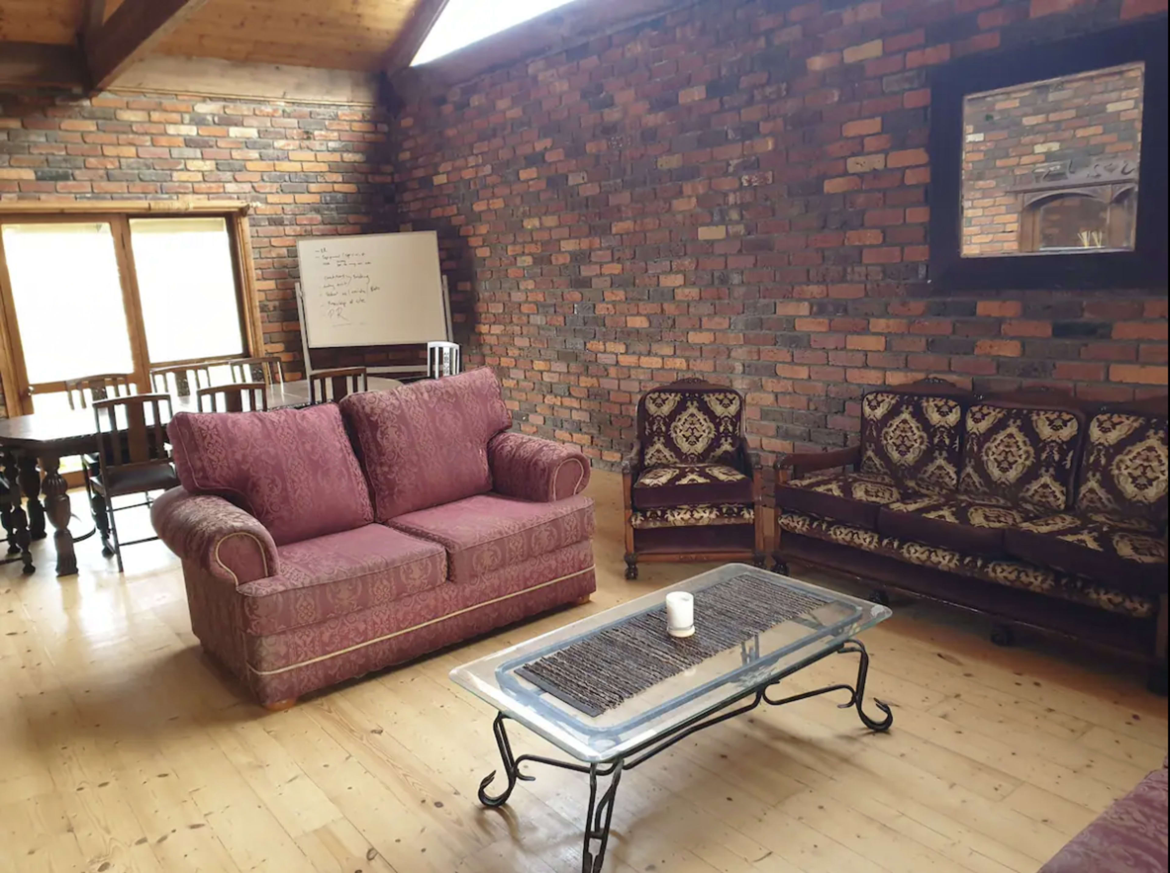 A living room with brick walls, wooden flooring, a glass coffee table, and a sofa set arranged around it.
