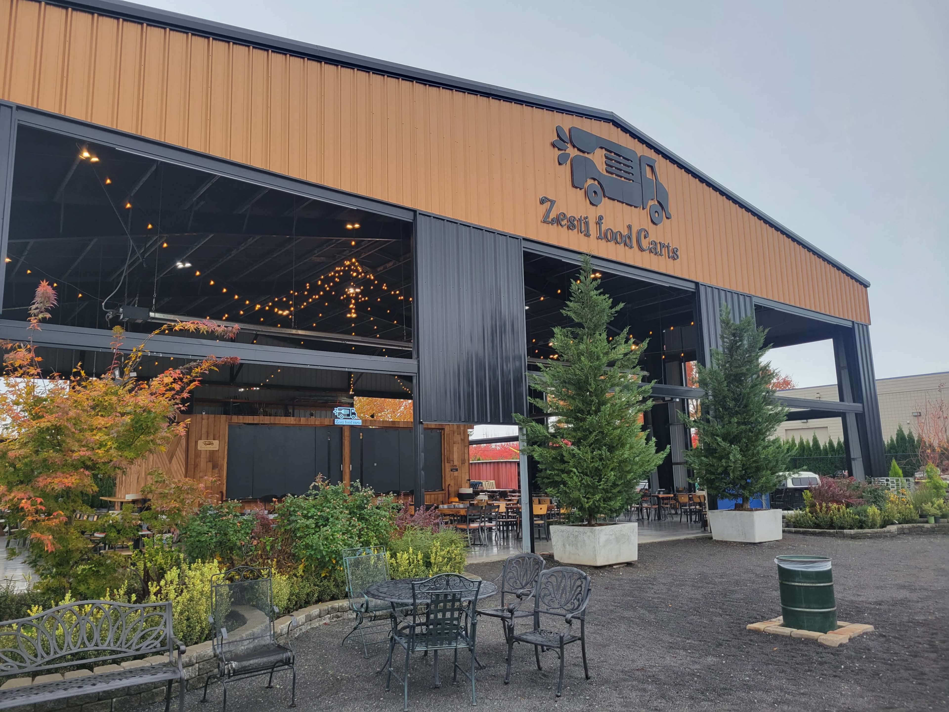 A large food cart area with a covered structure, featuring string lights and outdoor seating surrounded by greenery.