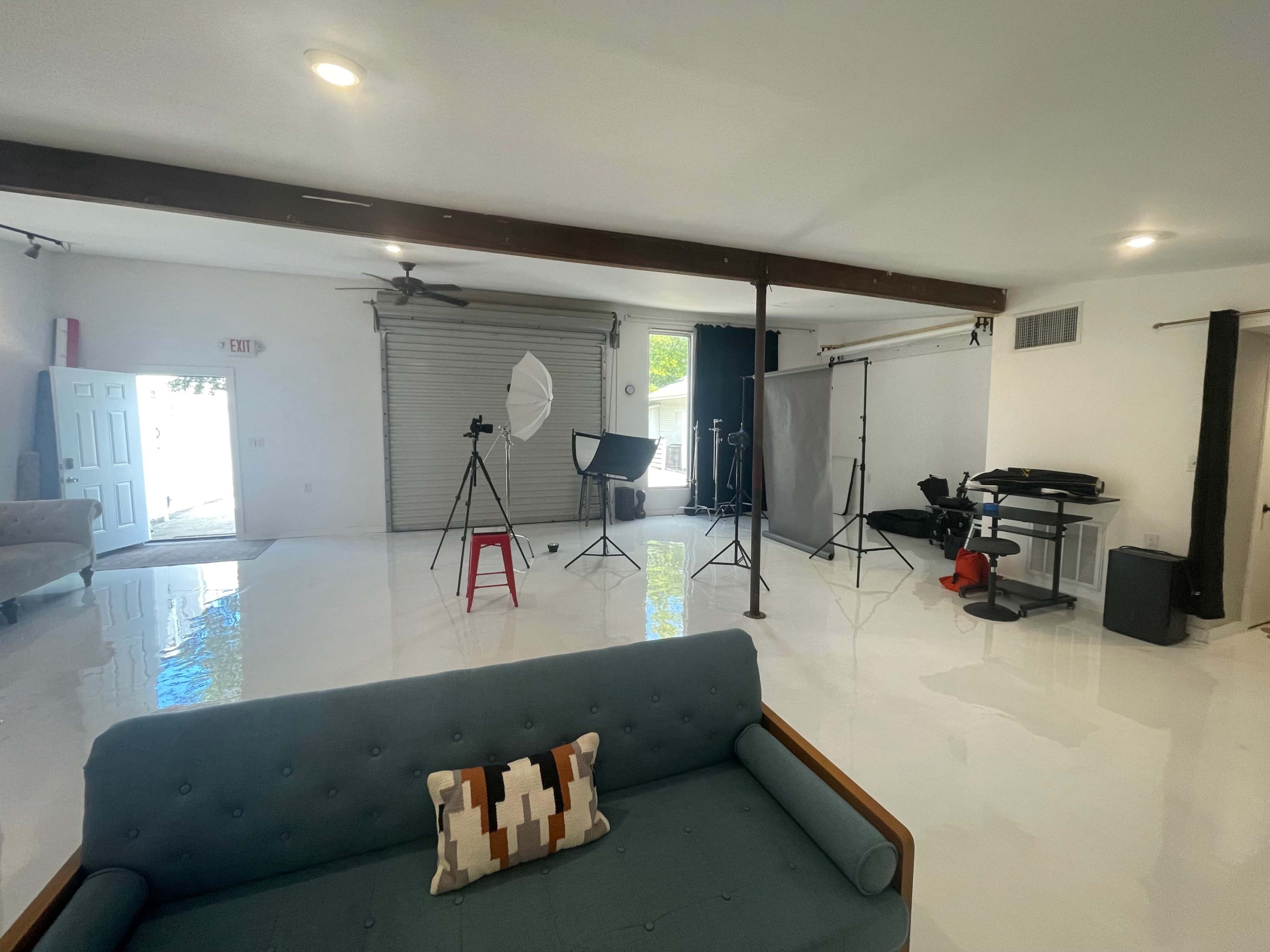 A bright studio space with a couch, photography equipment, and a garage door on one side.