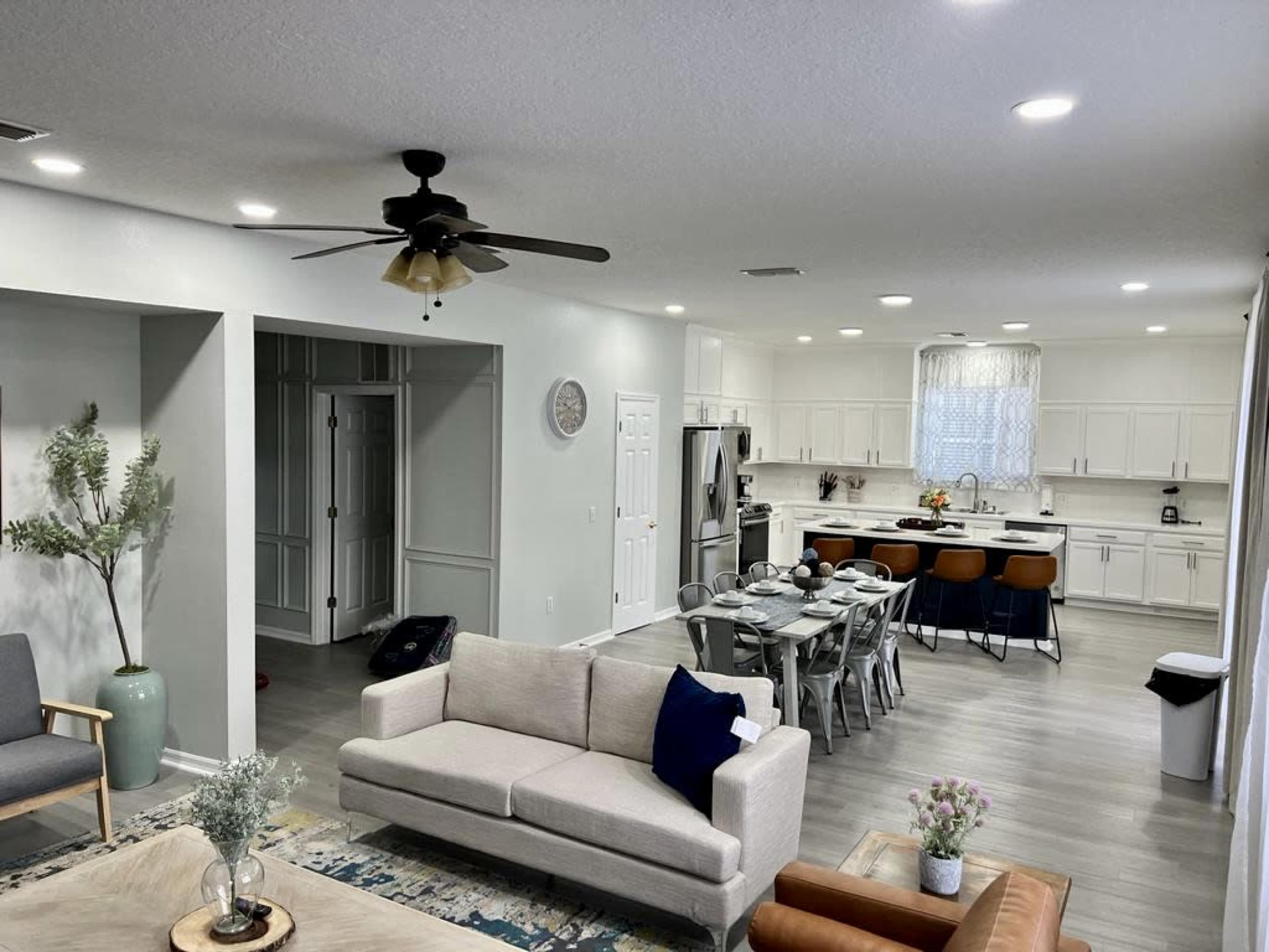 The image shows a modern, open-concept living area with a kitchen, dining table, and seating arrangements.