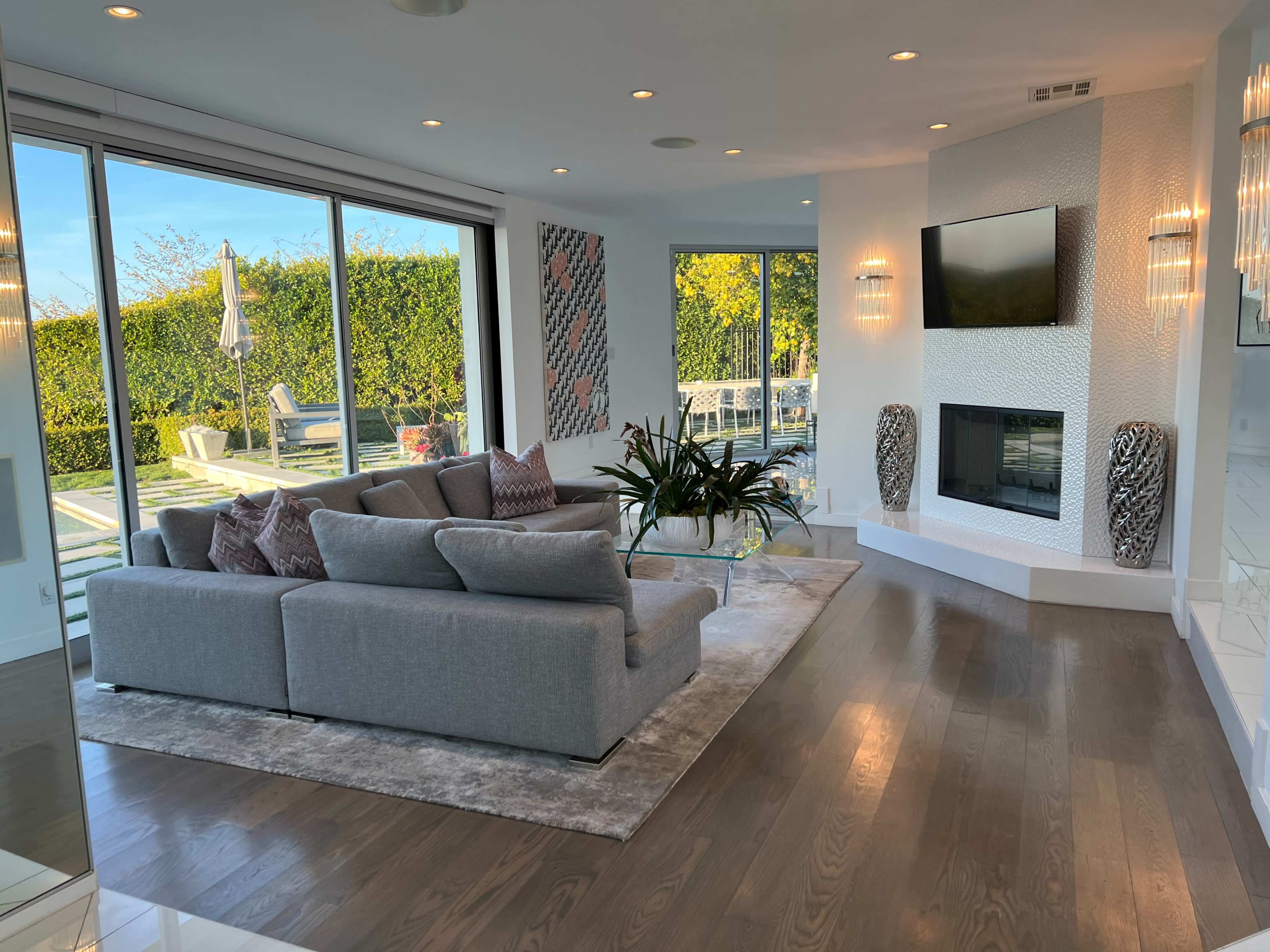 A modern living room with large windows, a fireplace, and a comfortable gray sectional sofa positioned on a light-colored rug.