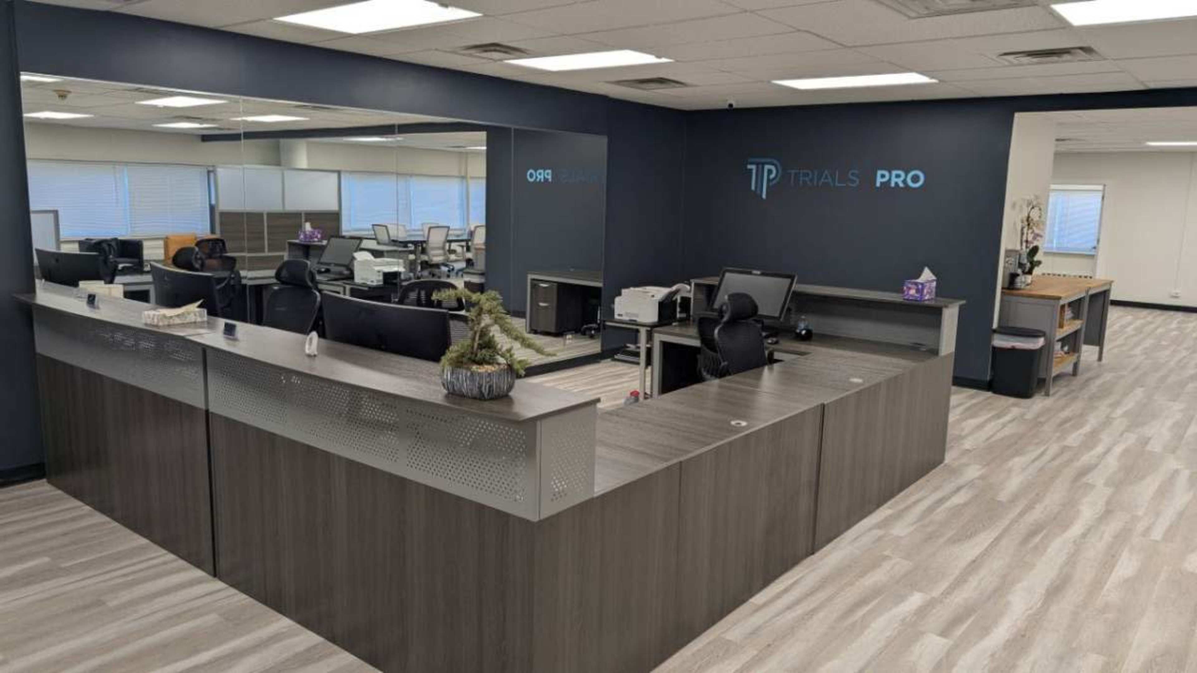 The image shows a modern office reception area with a large front desk, several workstations, and a mirrored wall.