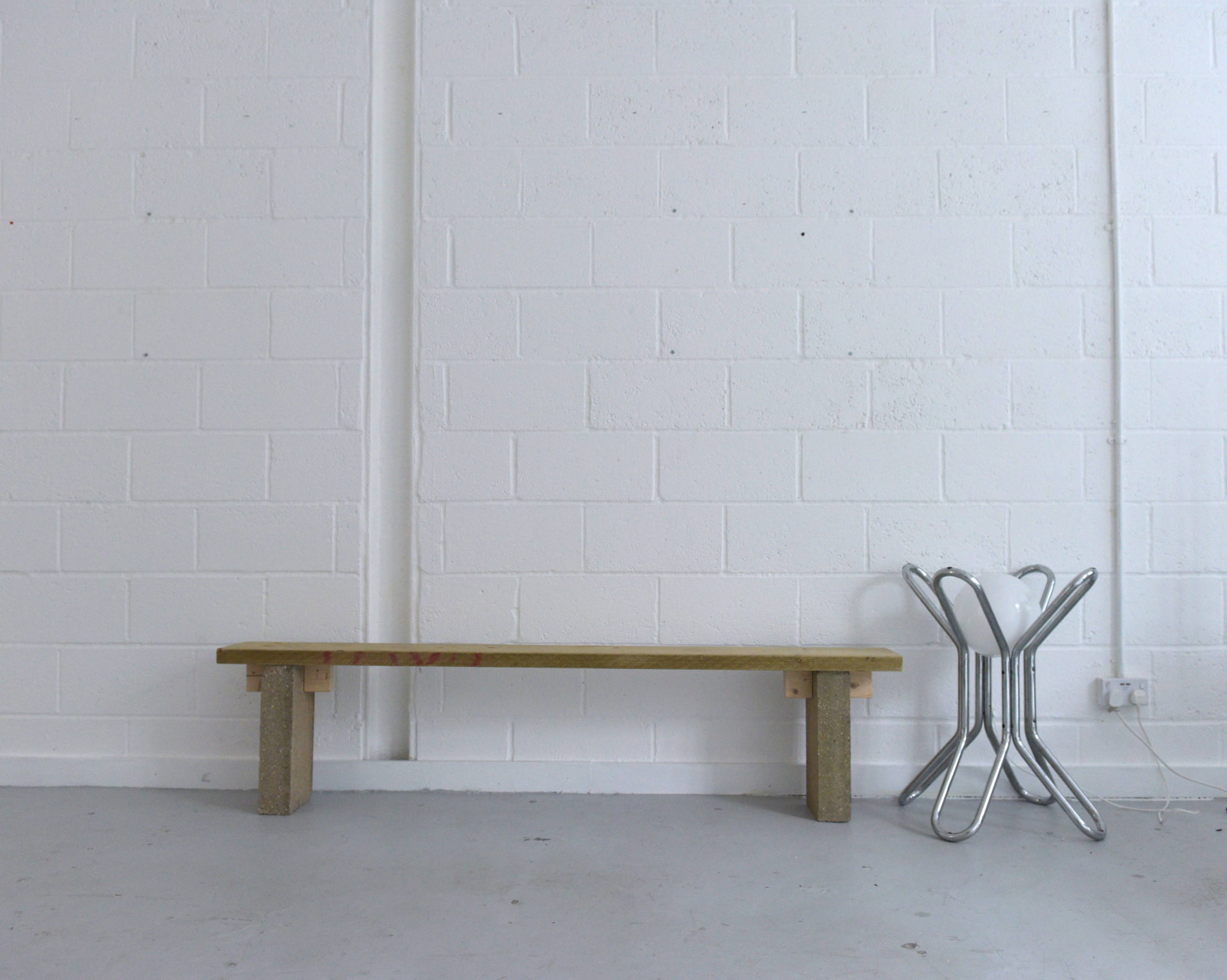 A wooden bench placed against a white brick wall, with a metal stool beside it.