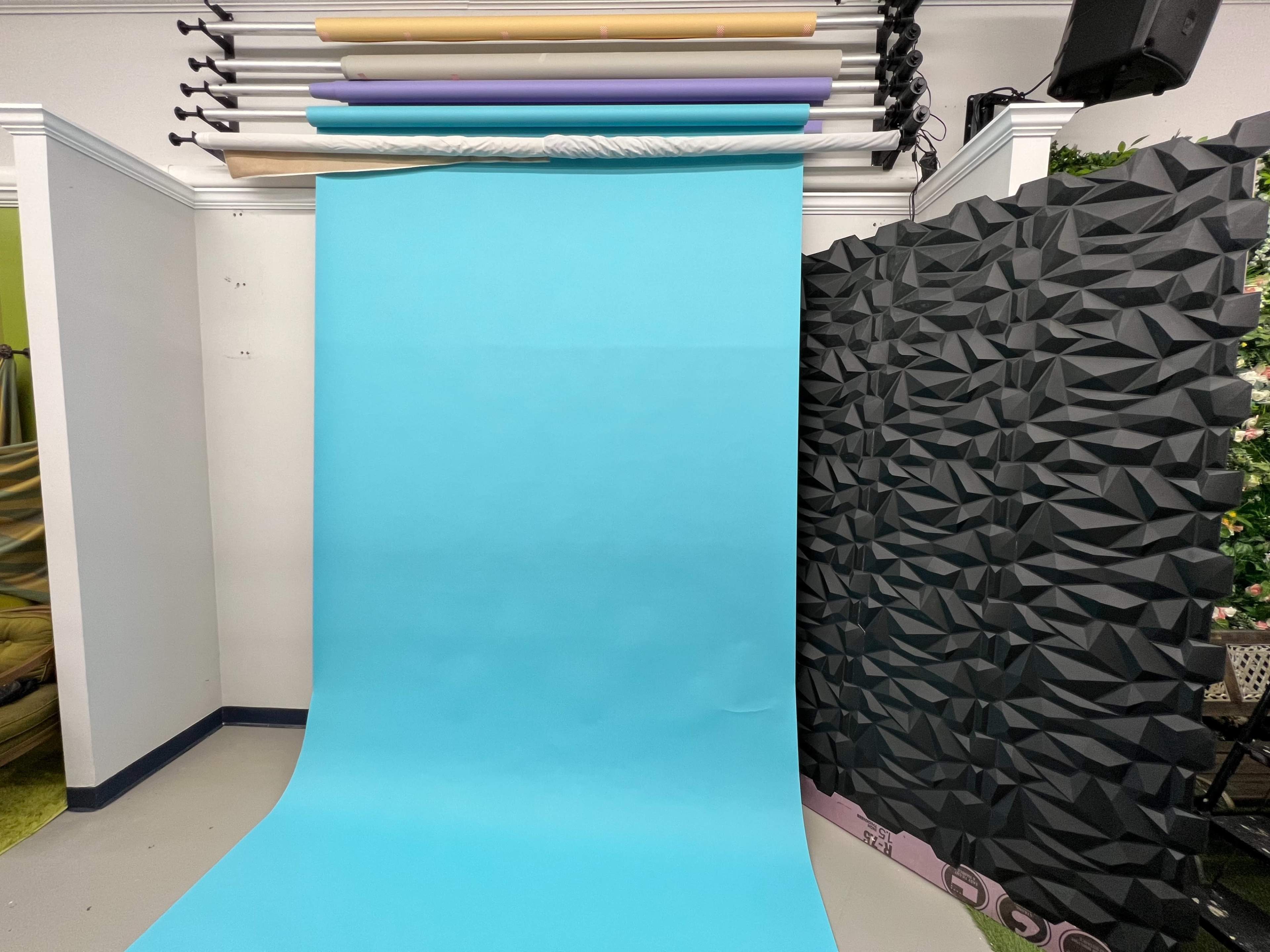 A photography studio with a large light blue backdrop and a textured black wall on the side.