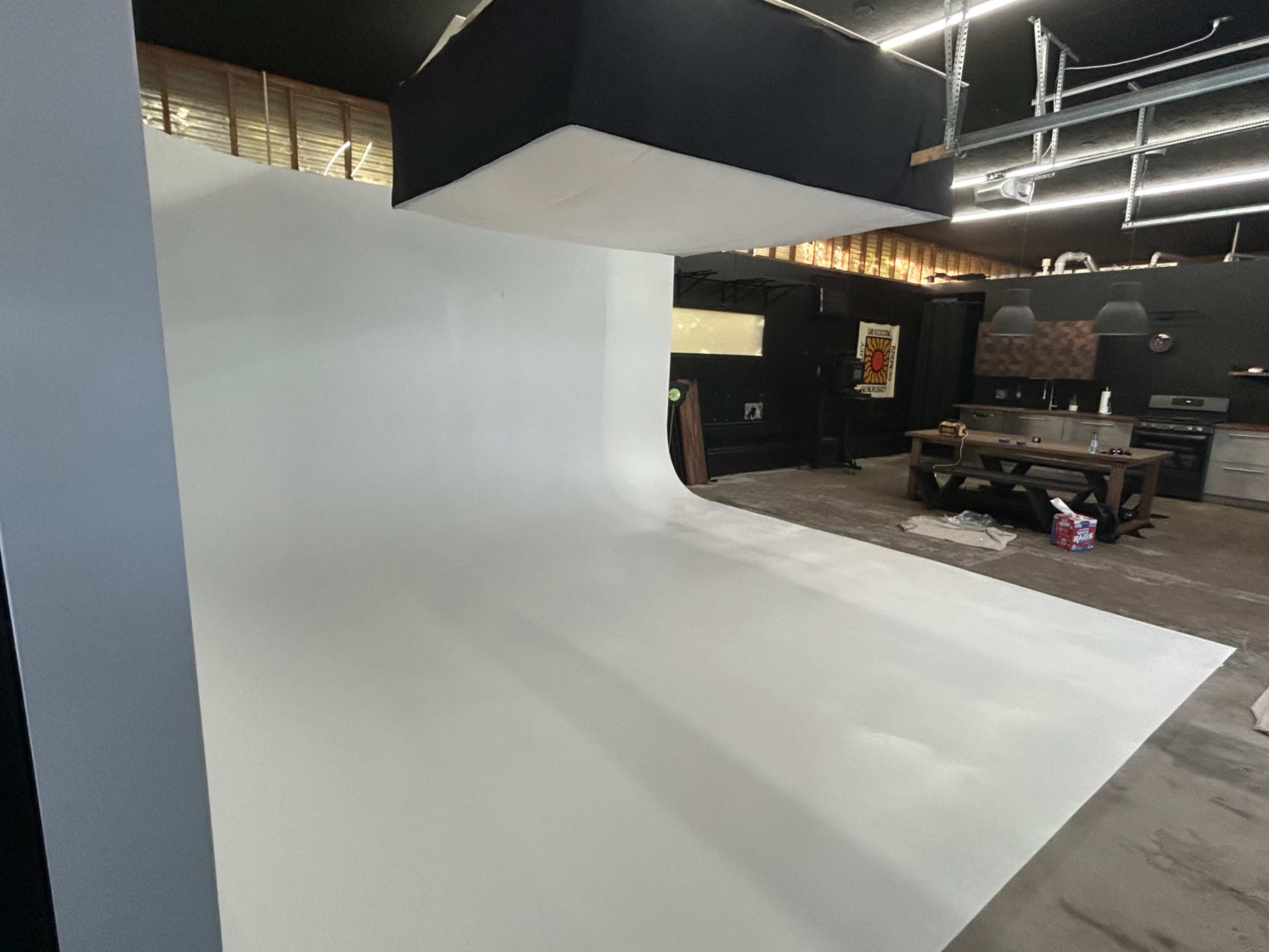 The image shows a photography studio with a large curved white backdrop and industrial-style lighting fixtures.