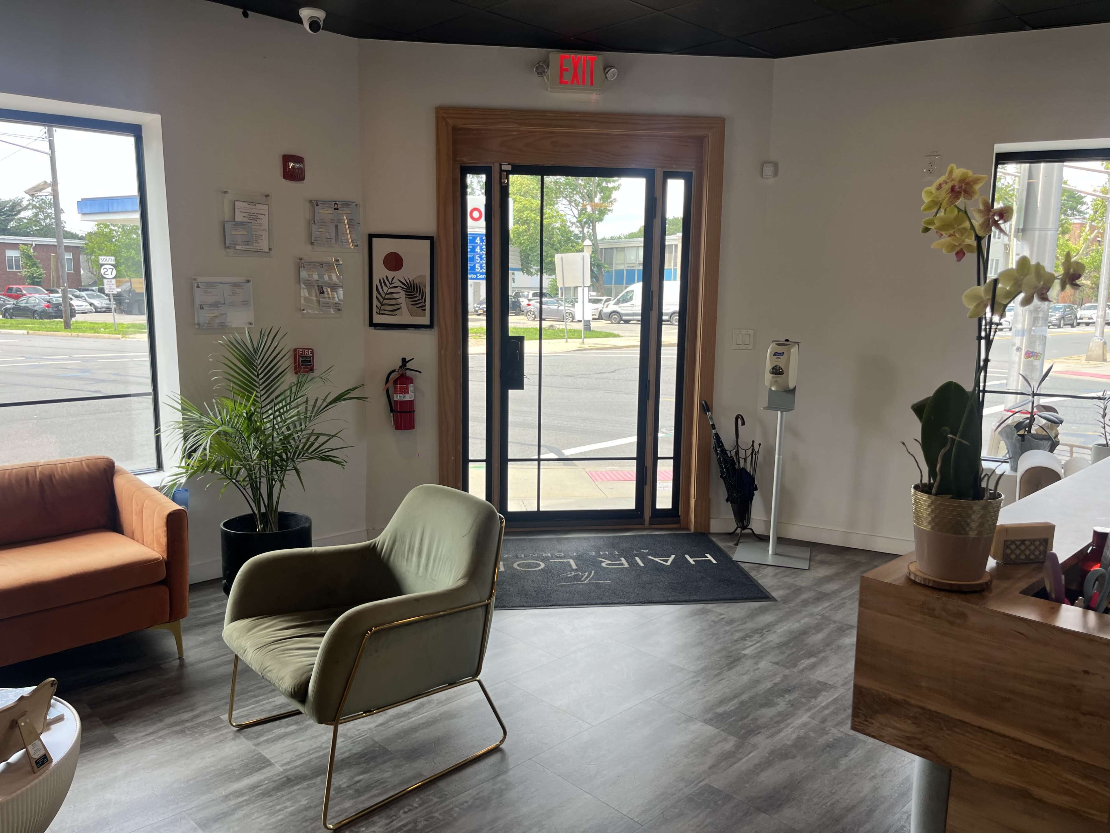 The image shows a modern waiting area with a green chair, an orange couch, and a reception desk near large windows facing a street.