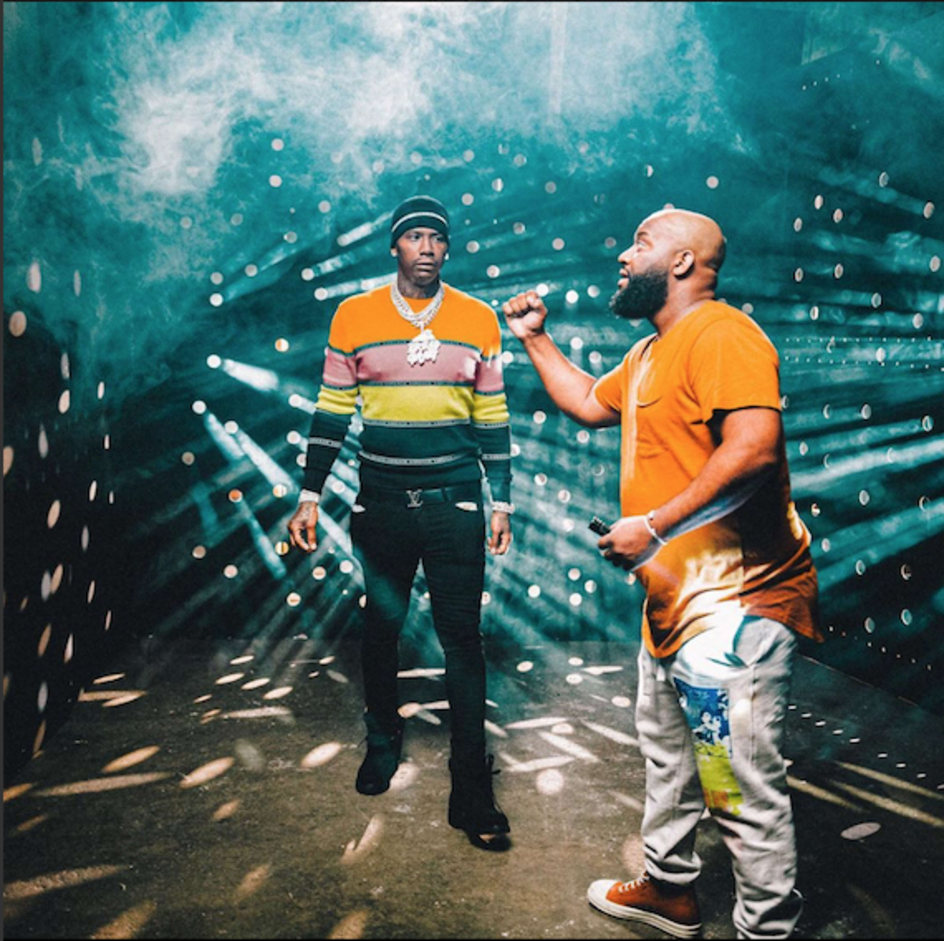 Two men stand in a smoky, illuminated space with beams of light radiating from various angles.