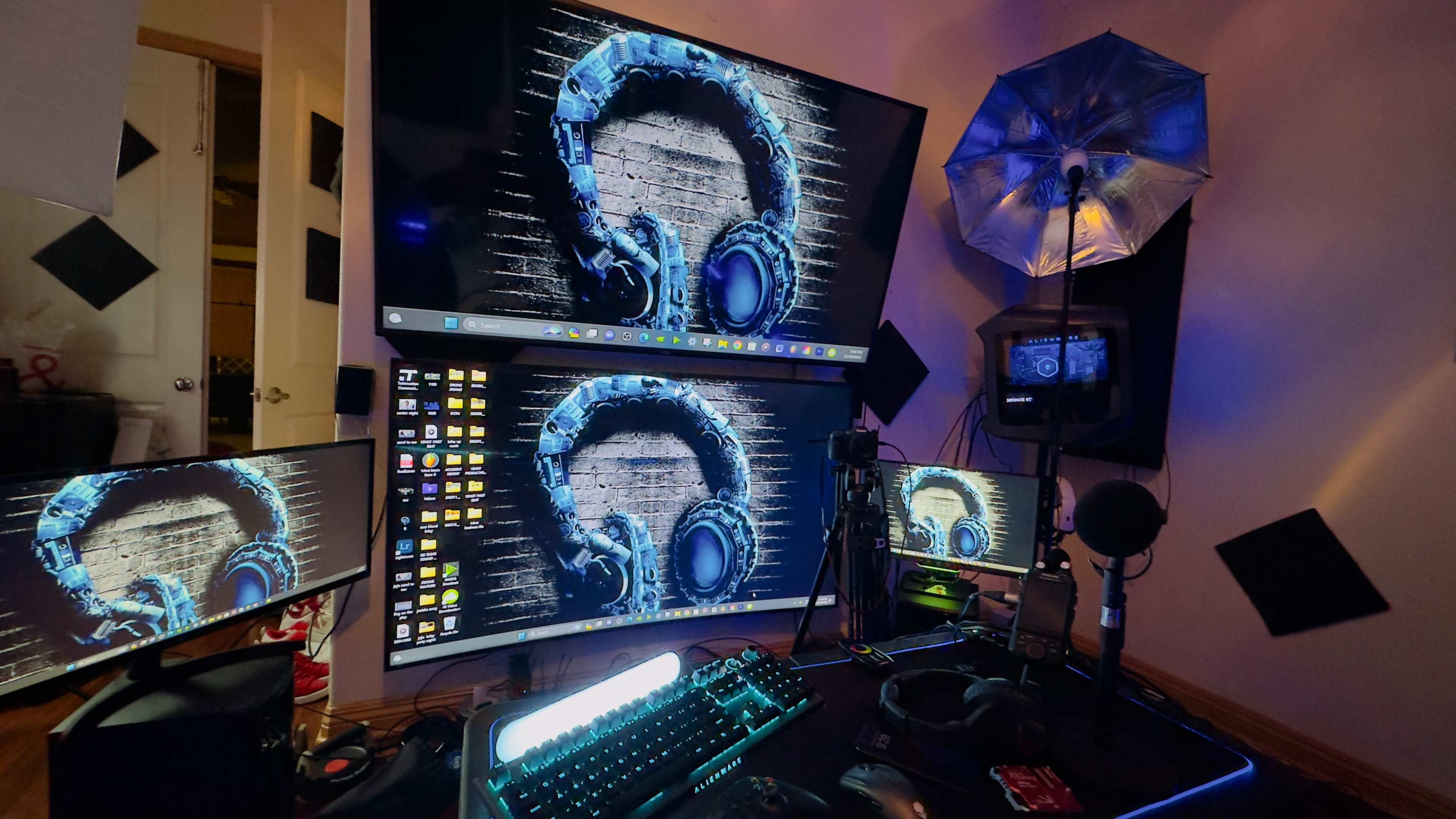 The image shows a multi-monitor computer setup featuring graphic designs of headphones on the screens, accompanied by a microphone and light umbrella.