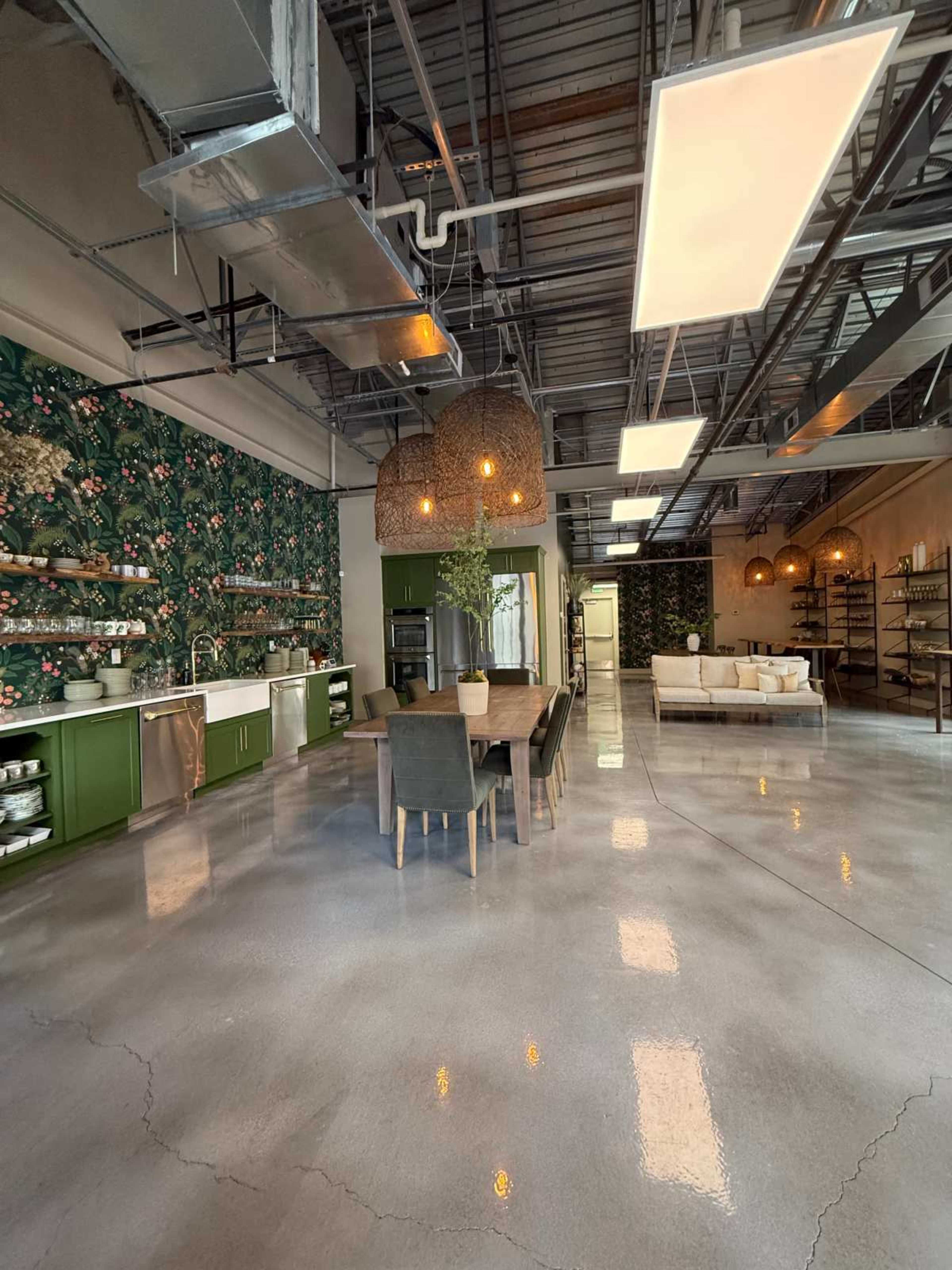The image shows a spacious kitchen and dining area with green cabinetry, a large wooden dining table, and decorative pendant lighting in a modern interior.
