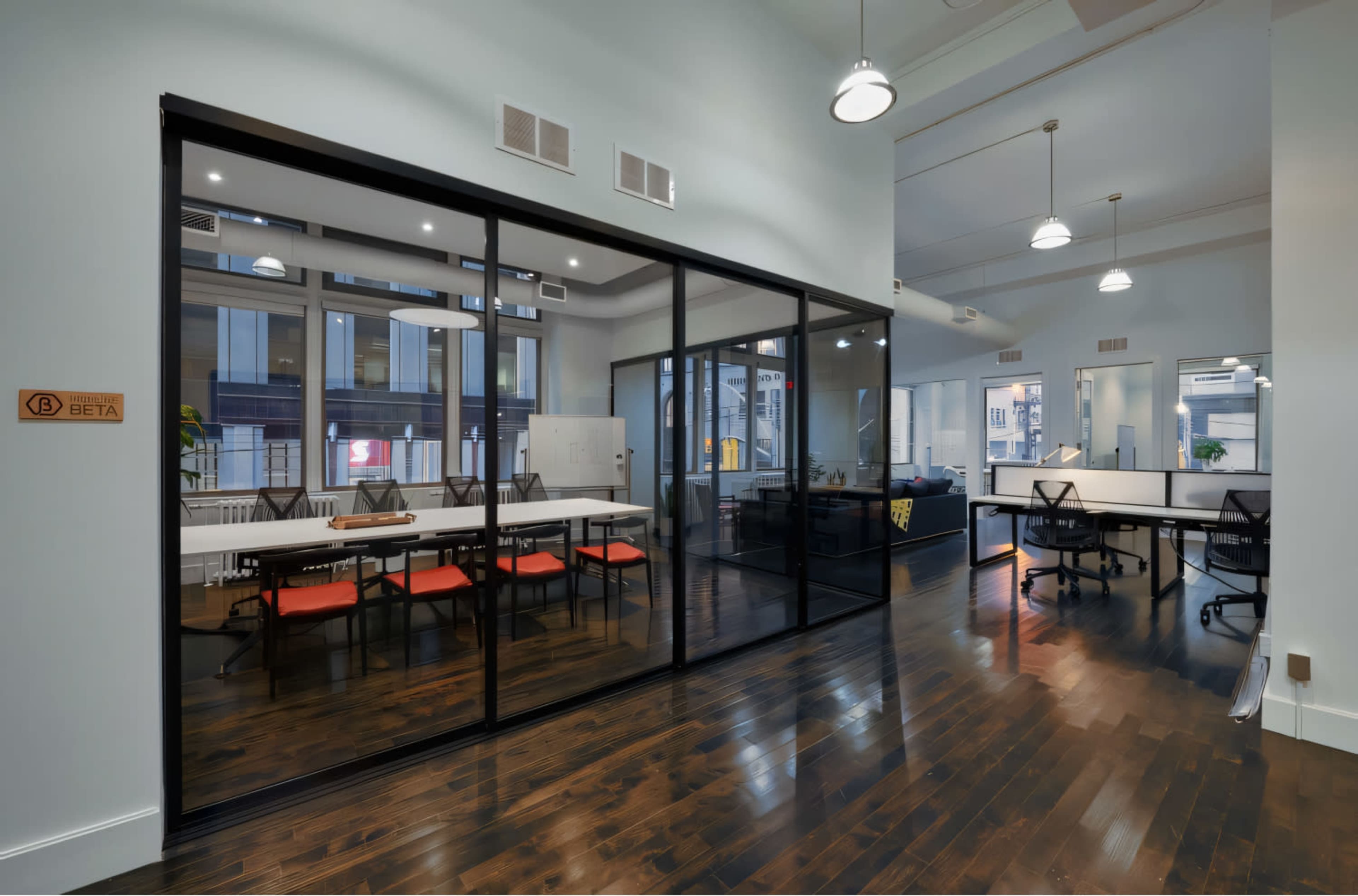 A modern office space with a glass-walled conference room and workstations, featuring hardwood floors and natural light from large windows.