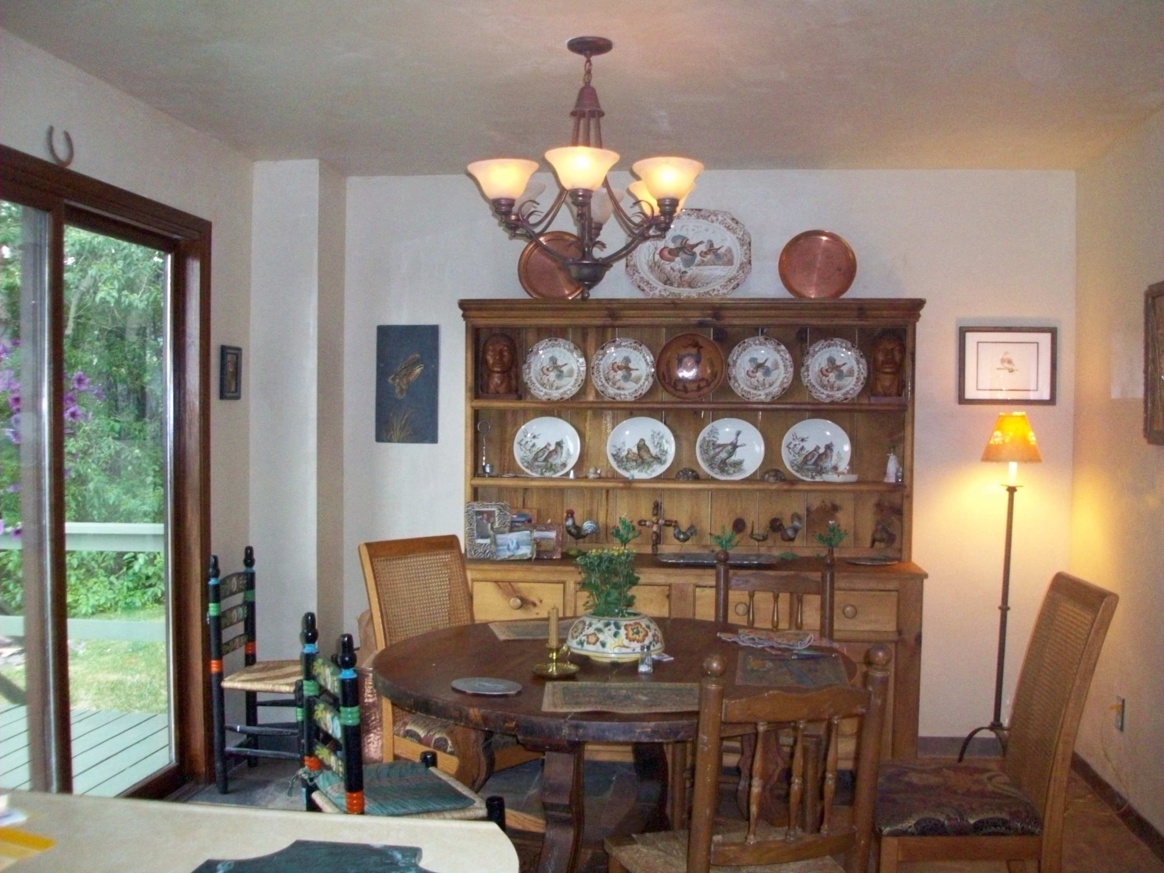 A dining area featuring a round wooden table, a china hutch displaying decorative plates, and a light fixture hanging from the ceiling.
