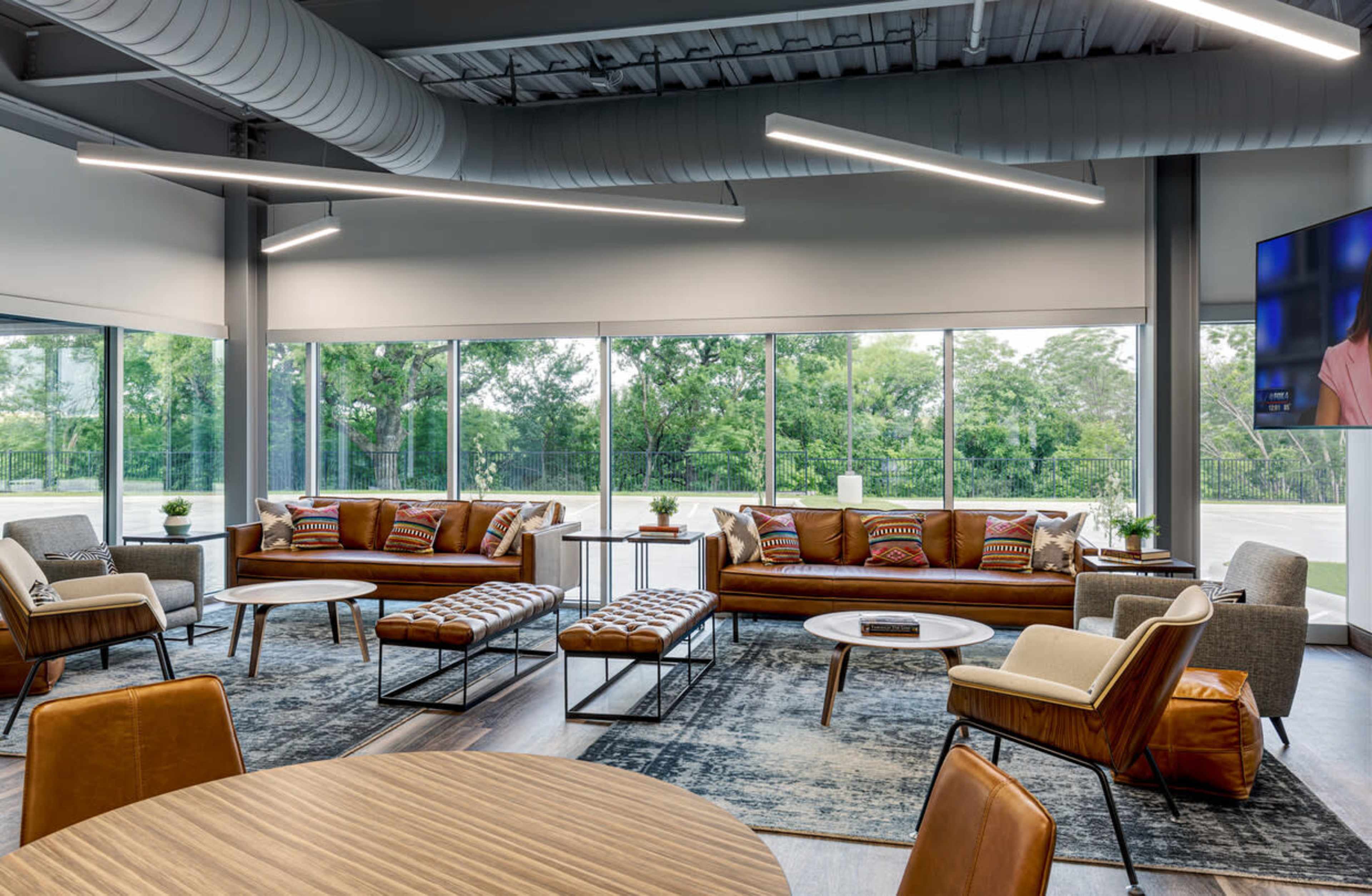 A modern lounge area with an arrangement of stylish sofas, chairs, and coffee tables, large windows offering a view of greenery outside.