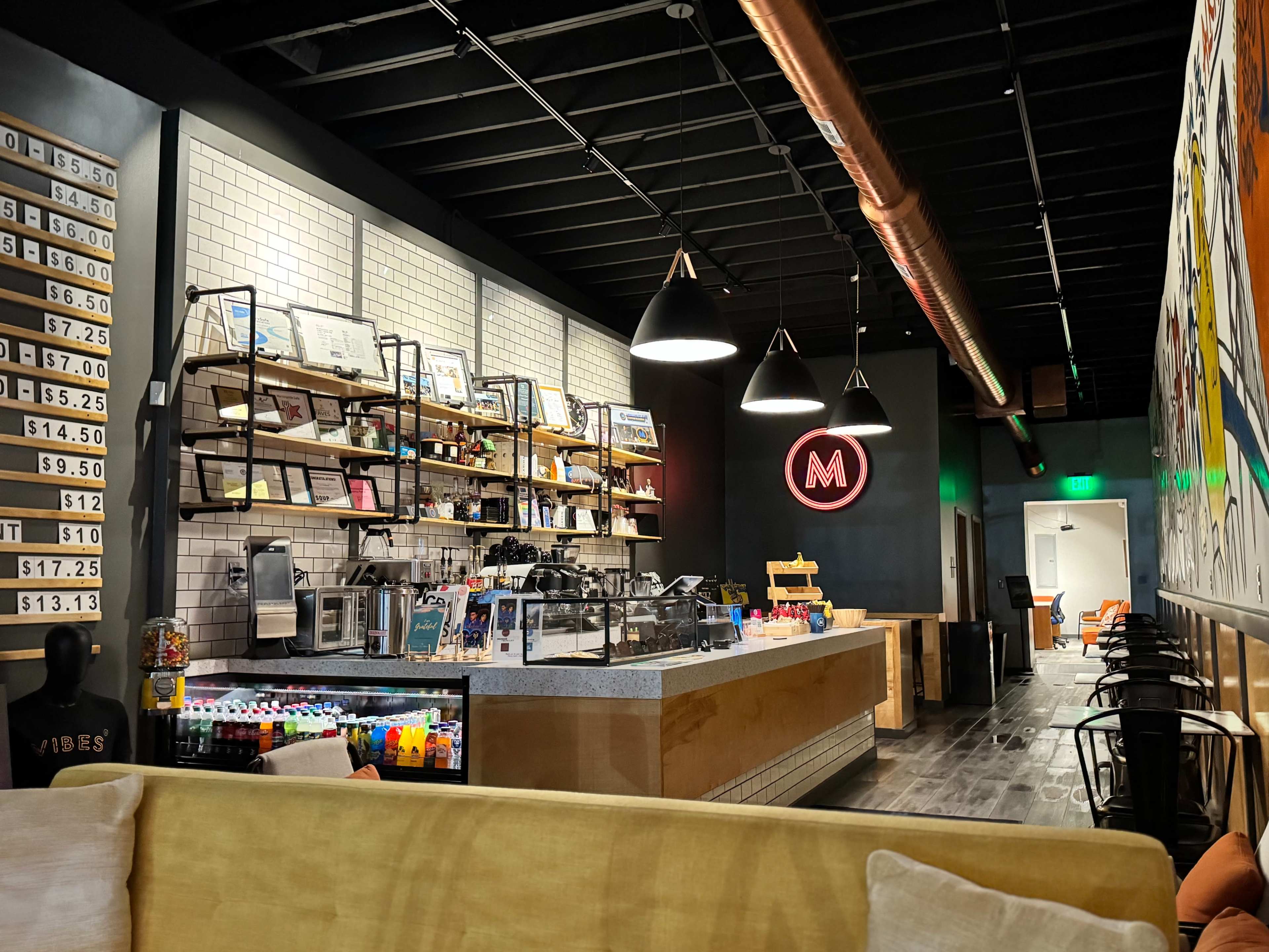 A modern café interior features a well-organized counter with shelving displaying drinks and snacks, complemented by stylish lighting and seating areas.