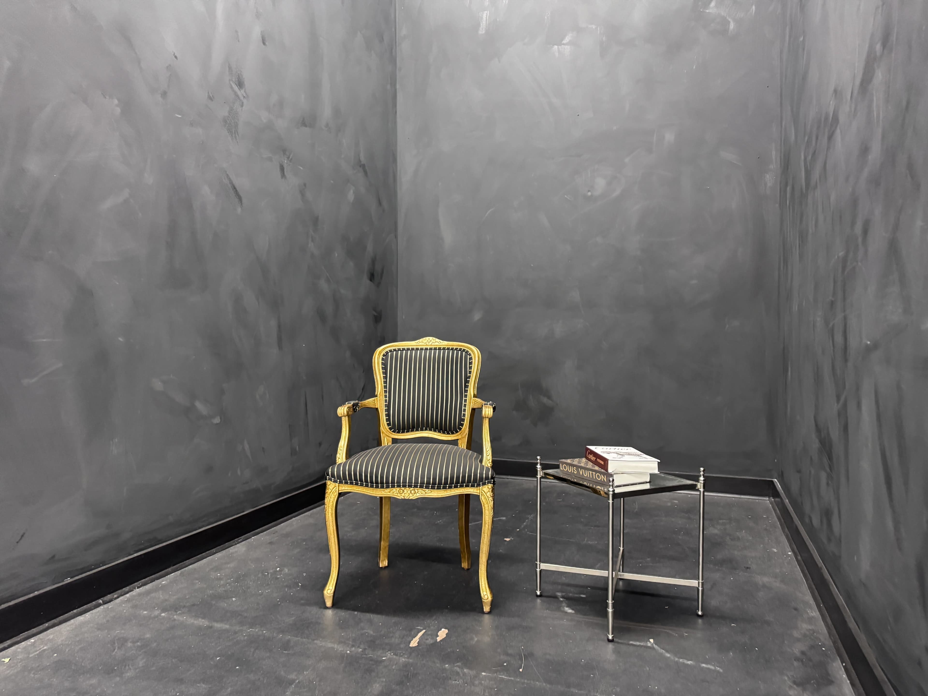 A yellow-accented chair sits next to a small table with books in a room with black walls.