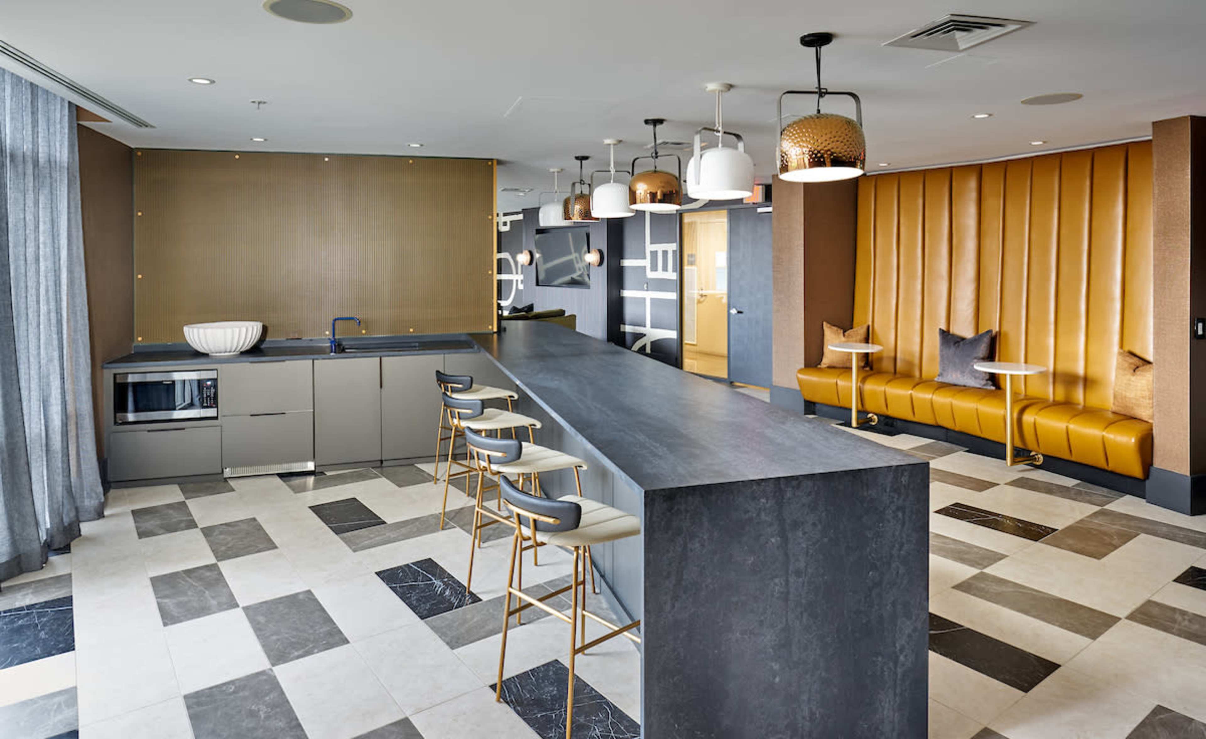 A modern kitchen features a long, dark countertop with bar stools, a microwave, and a seating area with yellow upholstered banquette.