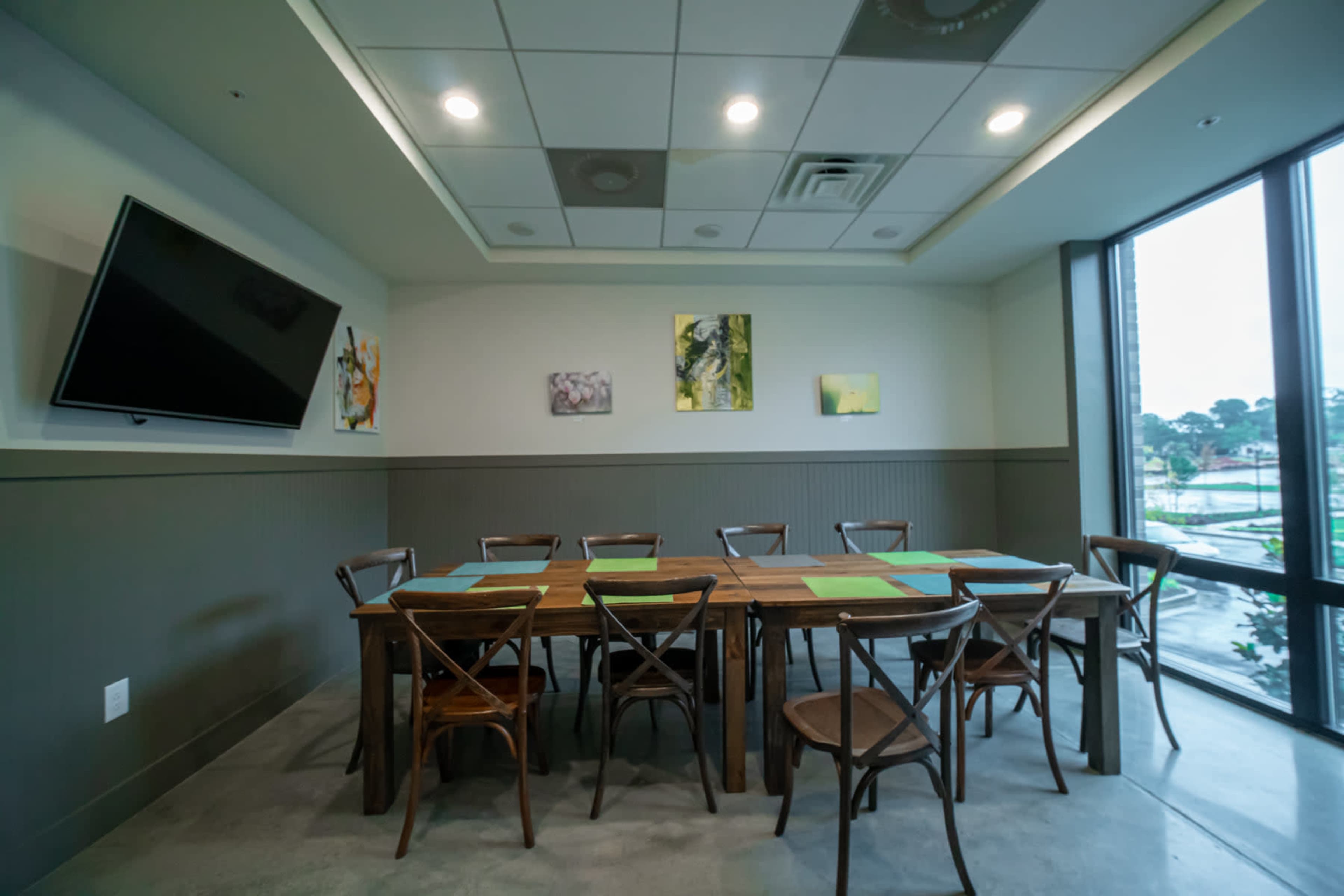 A dining area with a large wooden table surrounded by wooden chairs, a wall-mounted television, and artwork on the walls.