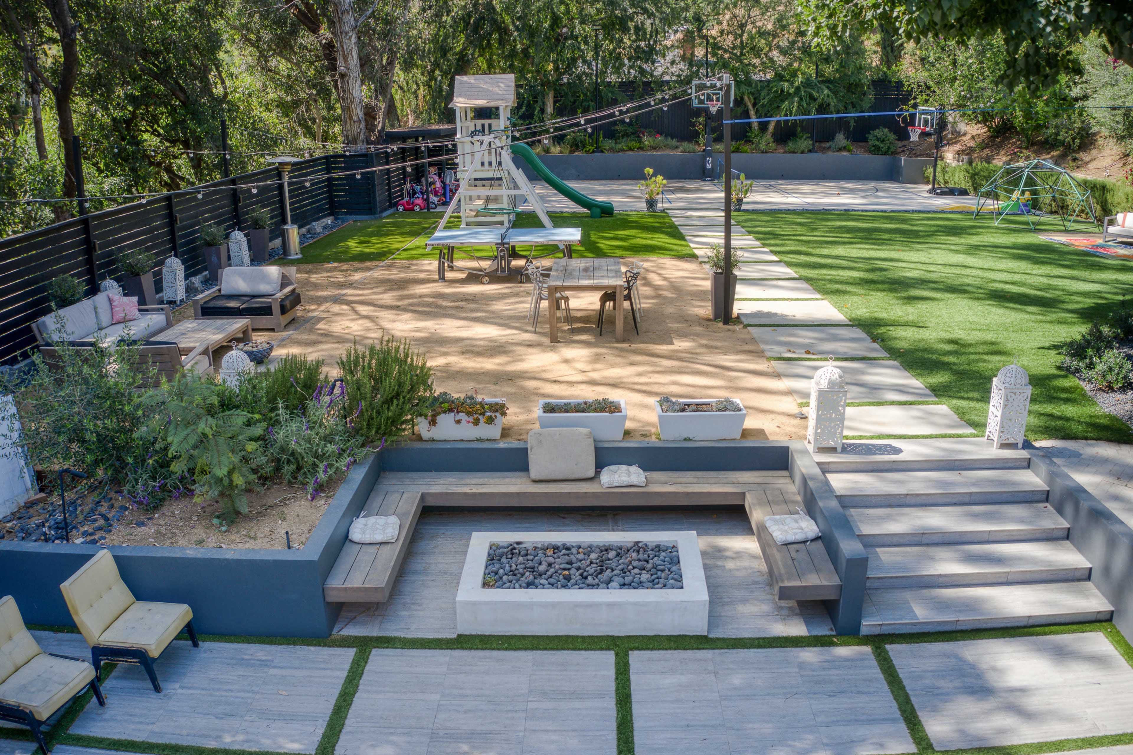 The image shows a landscaped outdoor space featuring a lawn, a playground structure, seating areas, and a fire pit.