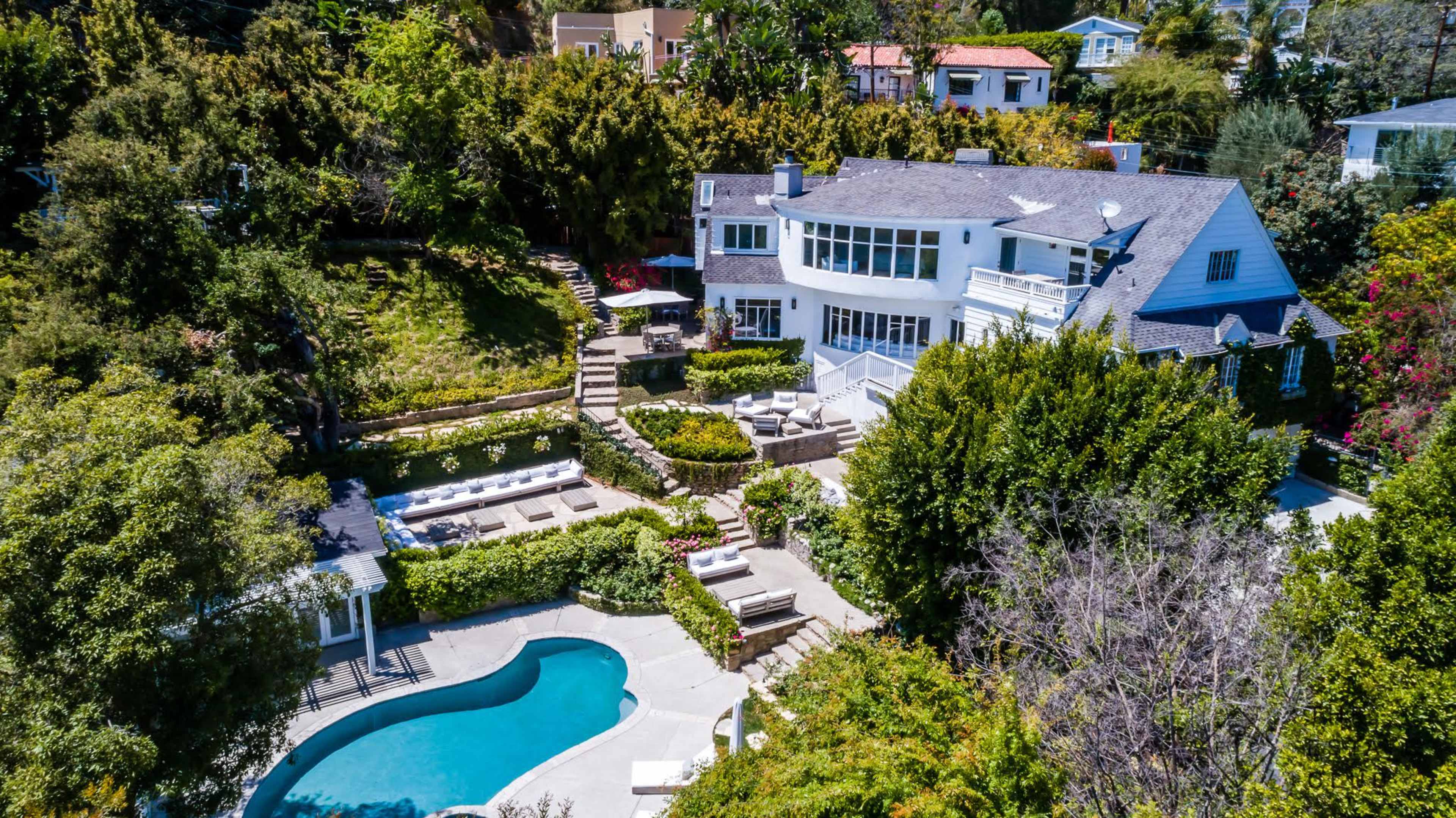 A spacious house with a swimming pool surrounded by landscaped greenery and outdoor seating areas.