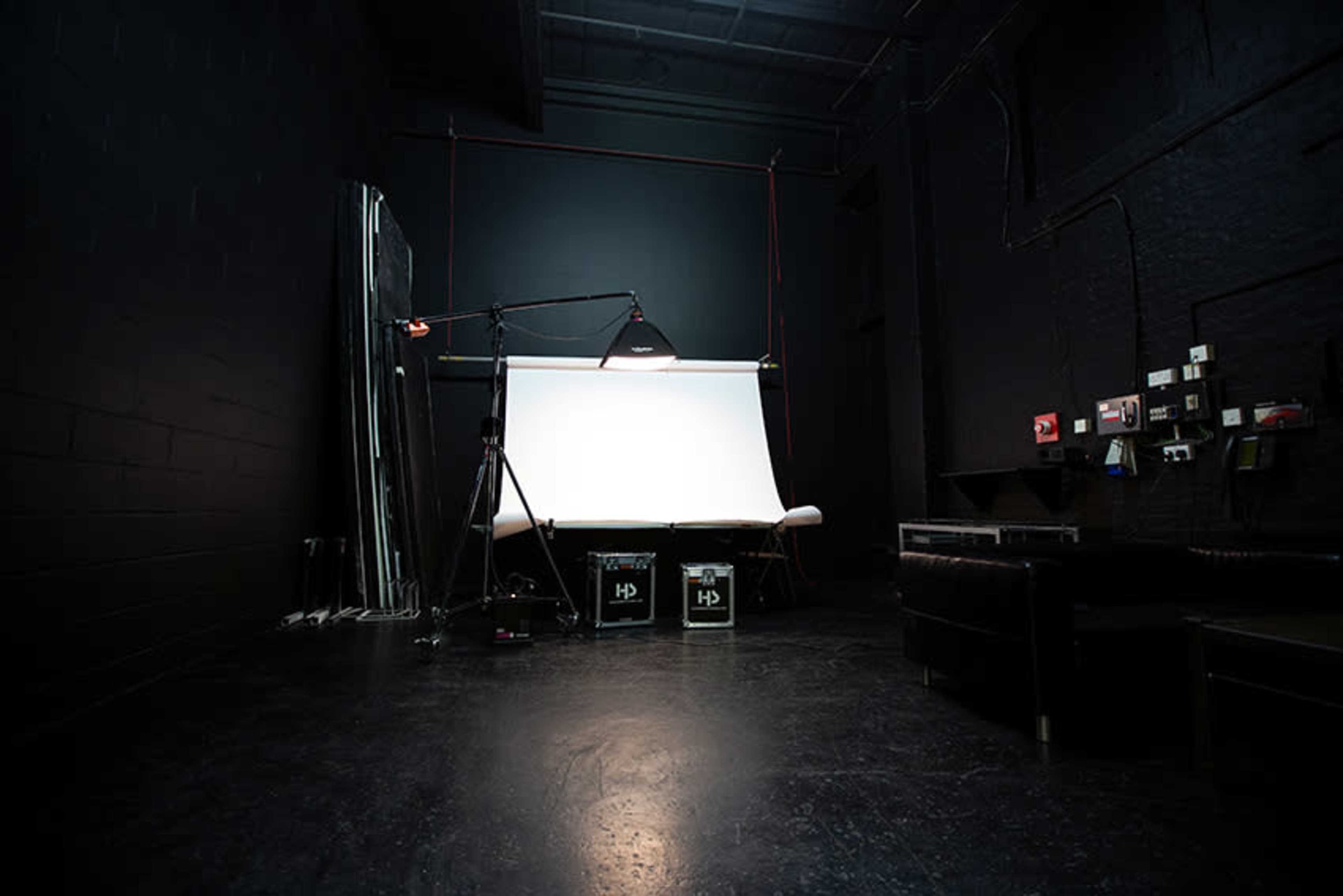 A dimly lit photography studio featuring a backdrop, lighting equipment, and storage boxes.