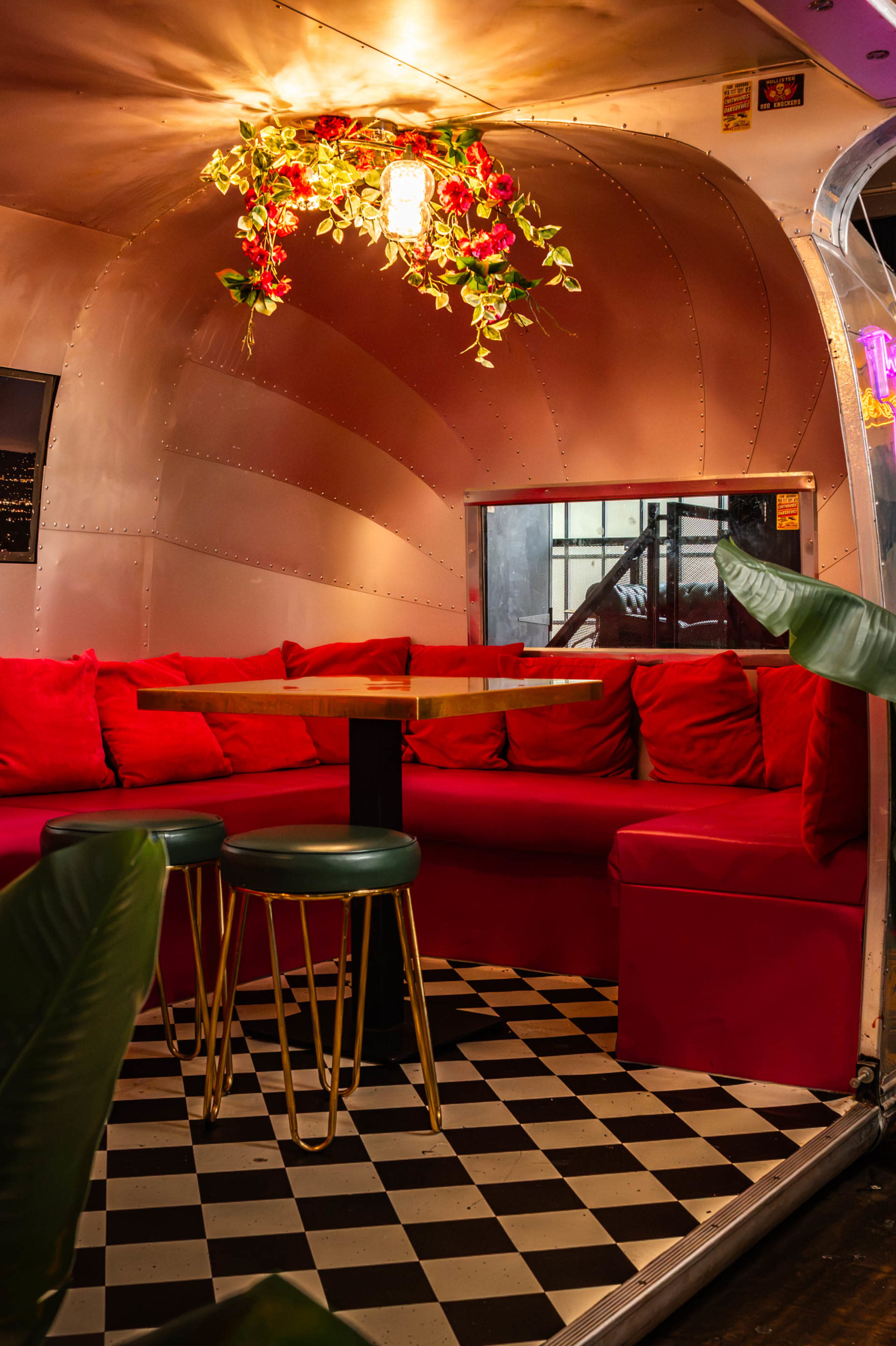 The interior of a cozy diner features a rounded metallic wall, a red couch with cushions, a wooden table, and checkered flooring.