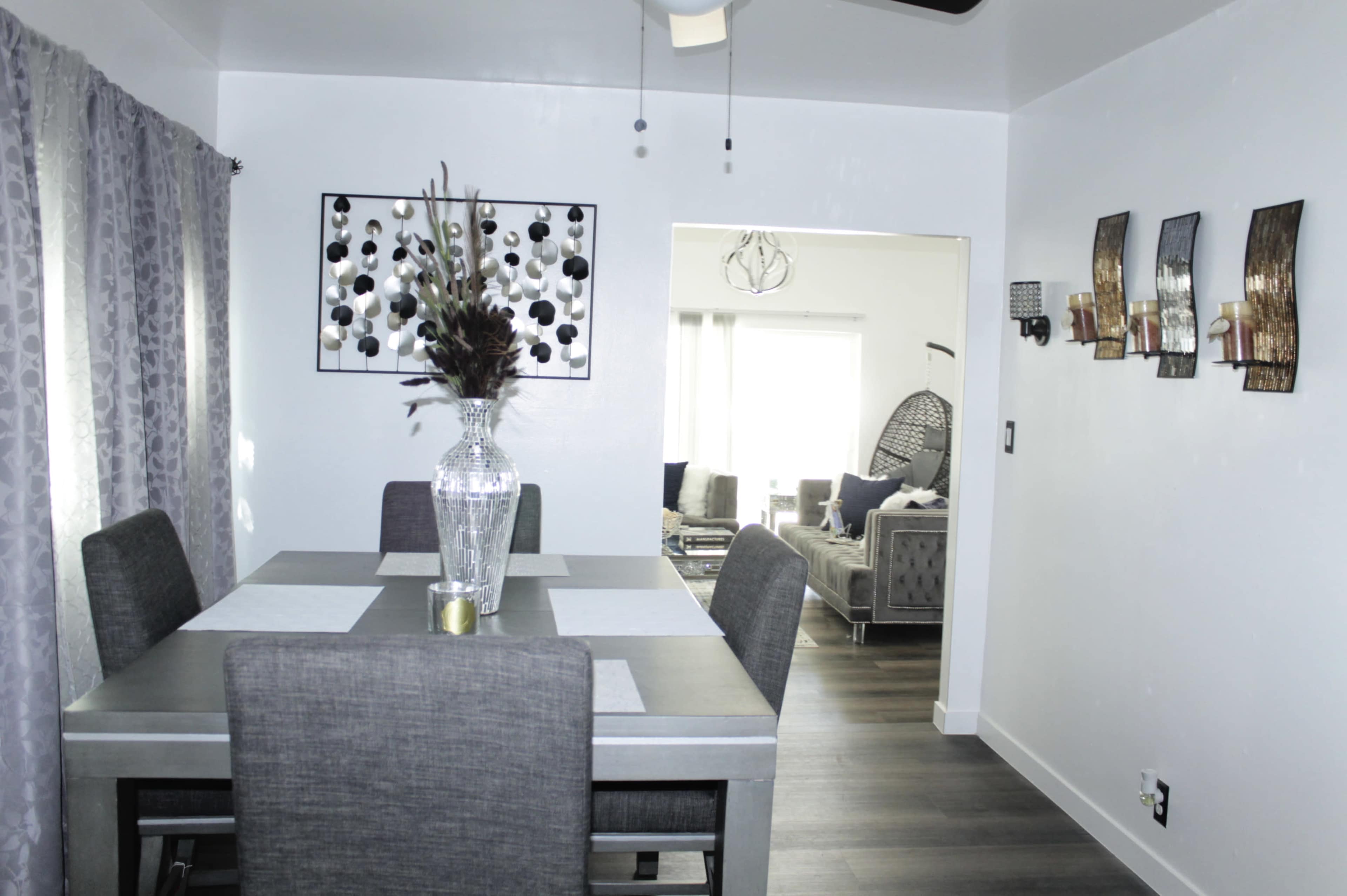 A dining area with a table set for six, featuring a vase of decor and a doorway leading to a living space.